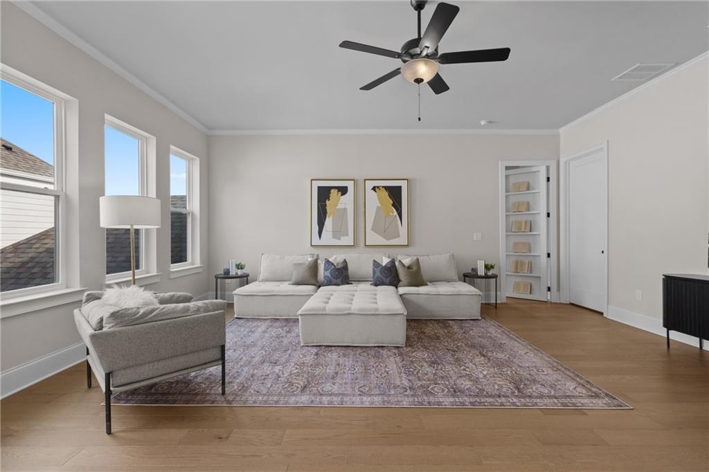 Cozy living room with beige L-shaped sofa, armchair, ceiling fan, abstract art, and hardwood floors in Davidson Homes The Seaside B, Woodstock, GA