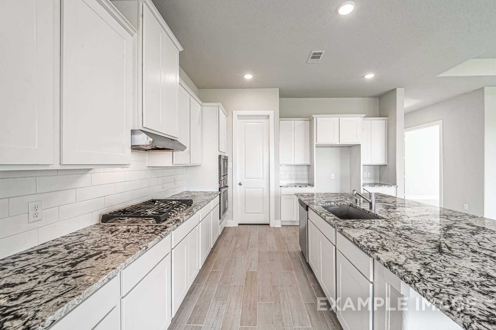 Spacious kitchen in The George B with white shaker cabinets, granite countertops, large island, and subway tile backsplash