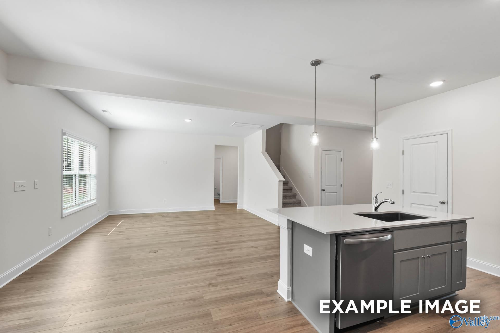 Open-concept kitchen-living space with central island, sink, dishwasher, hardwood floors, and staircase in The Shelby A, Hazel Green, AL