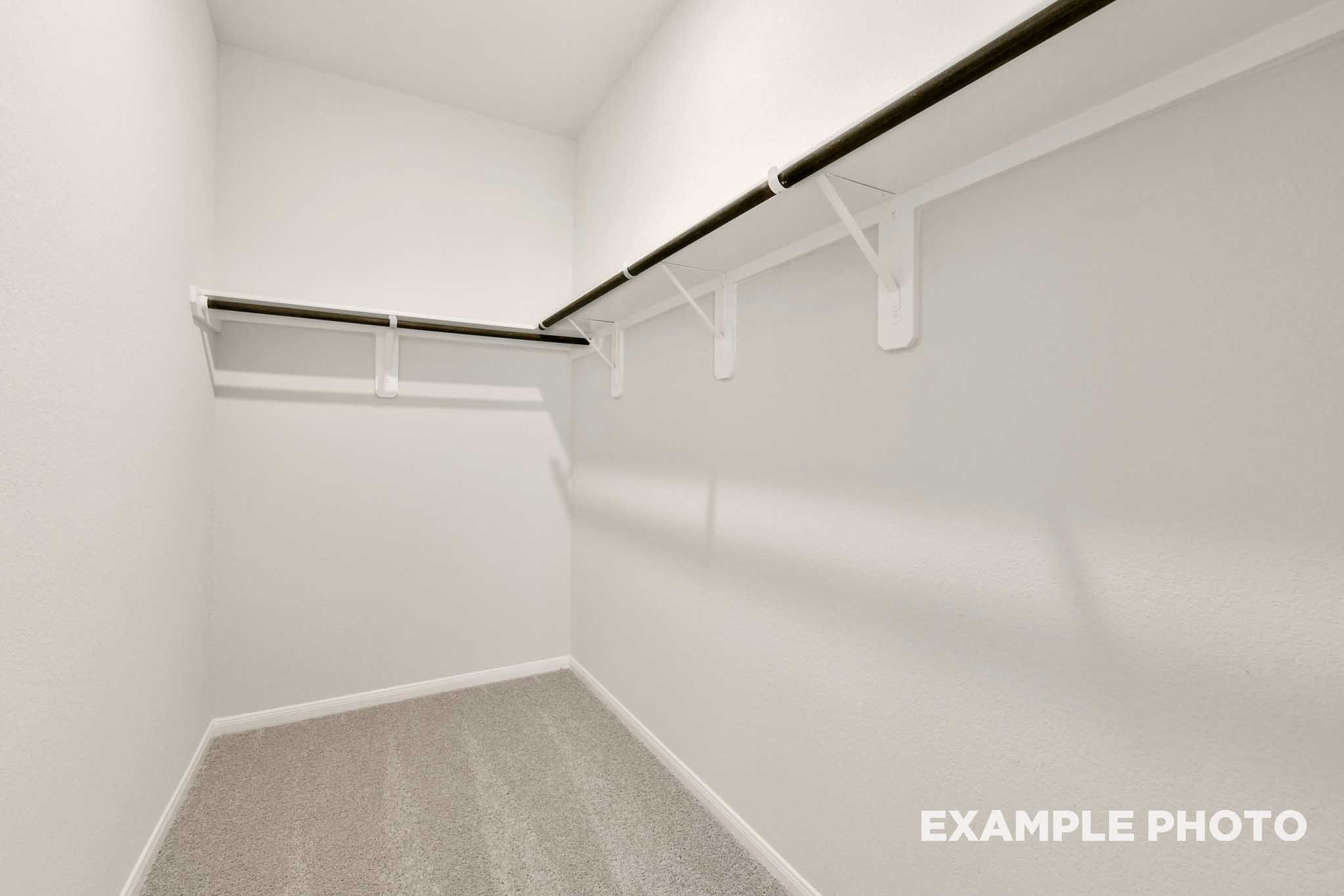 Spacious walk-in closet in The Frio master suite featuring white shelving and neutral carpeting.