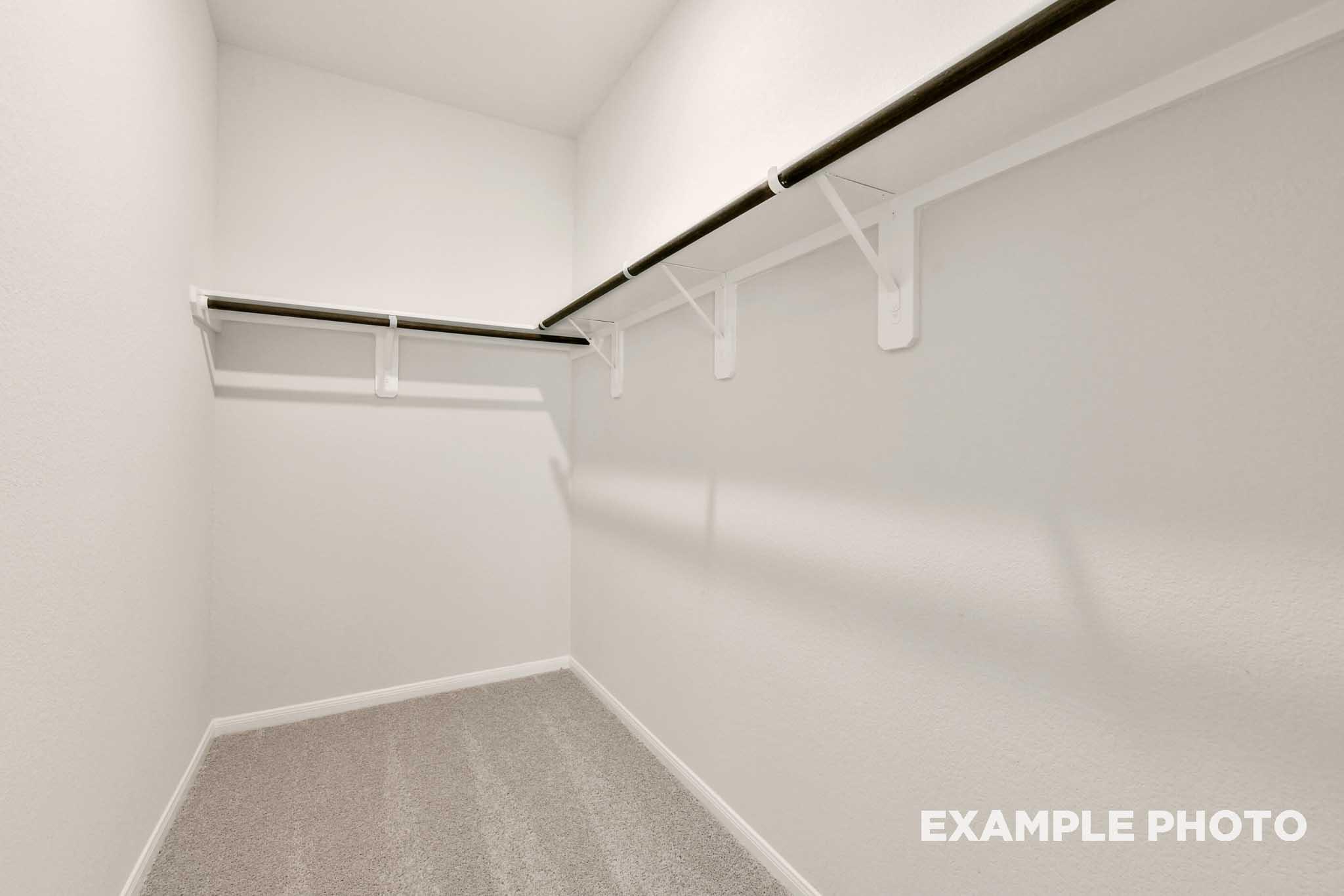 Spacious walk-in closet in The Frio master suite featuring white shelving and neutral carpeting.