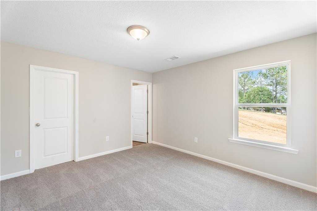 Spacious secondary bedroom with beige walls, carpet floor, double doors, and tree-view window in Evermore Homes The Washington, Phenix City