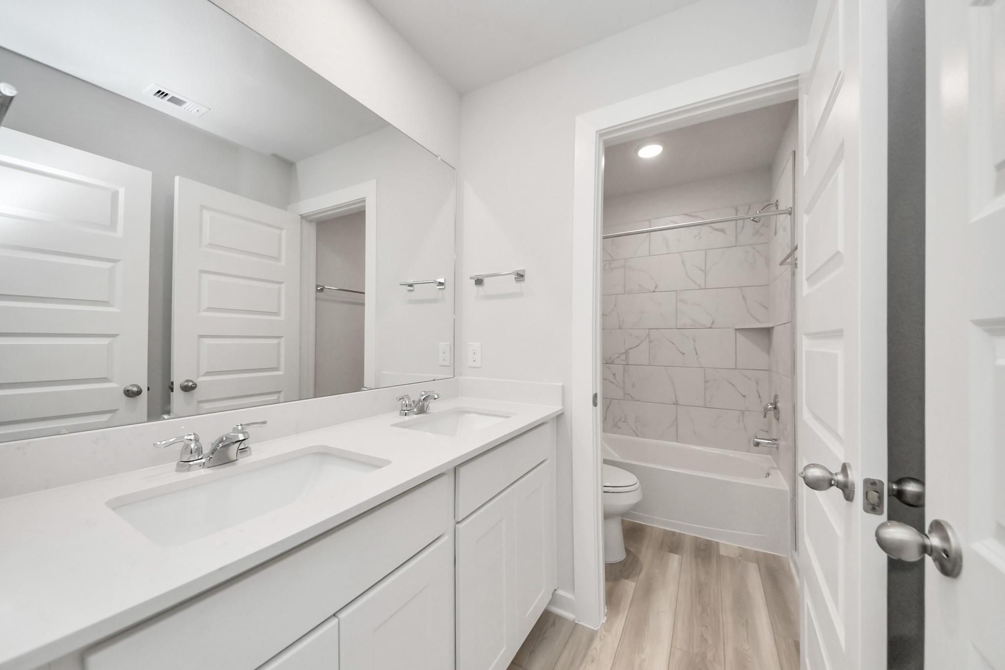 Modern bathroom with double vanity and tiled shower in The Sabine F floor plan at Liberty Estates, Cleveland, Texas.