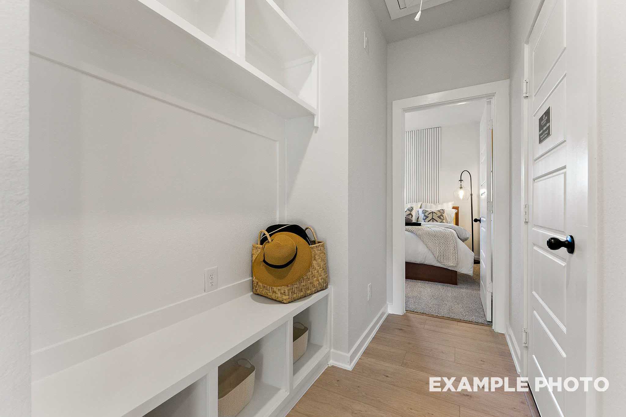 Spacious mudroom in The Everett home design featuring white built-in shelves, bench seating, wicker basket, and hallway to master bedroom