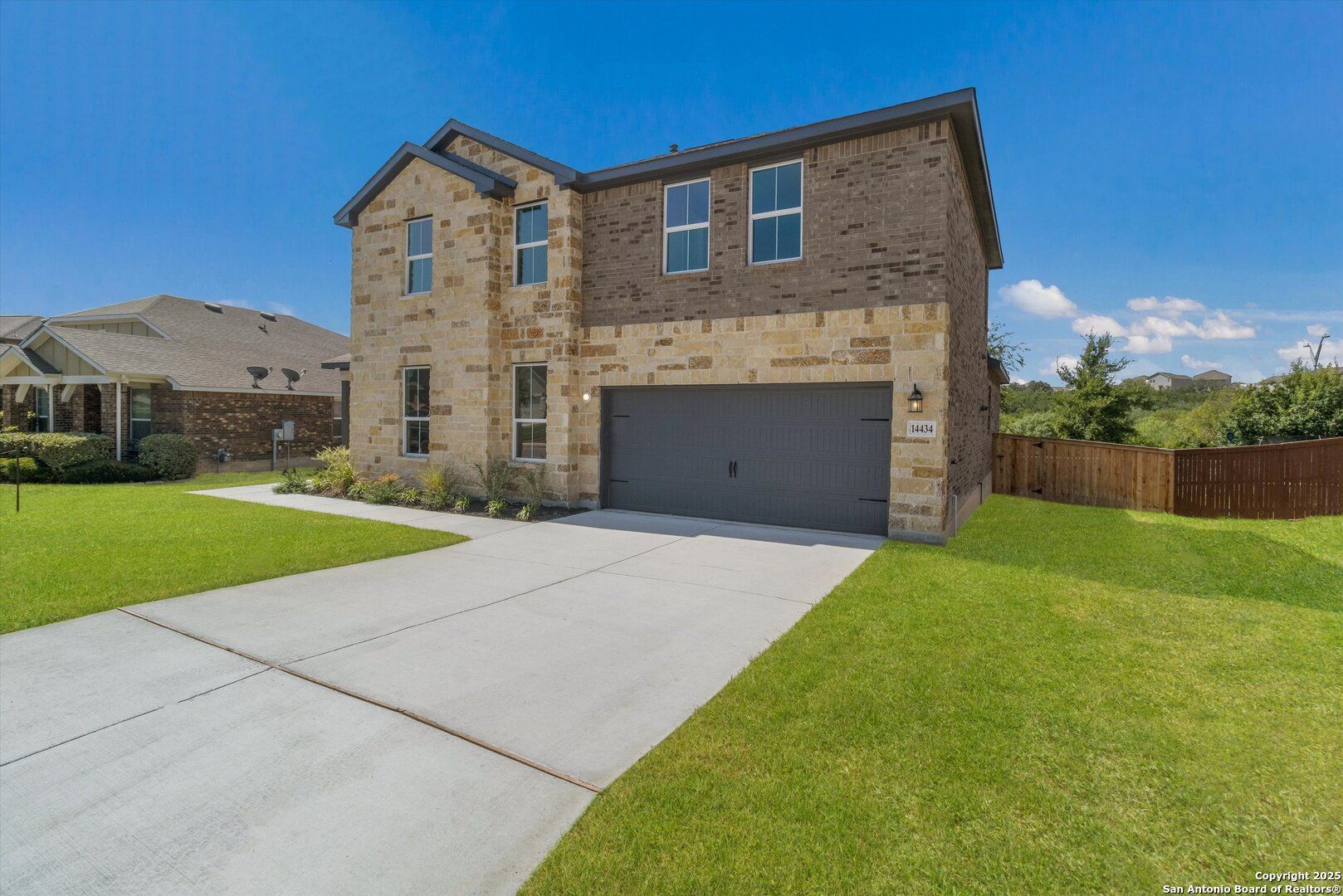 Modern two-story brick and stone home with two-car garage, driveway, and landscaped yard in Ladera, San Antonio, Texas