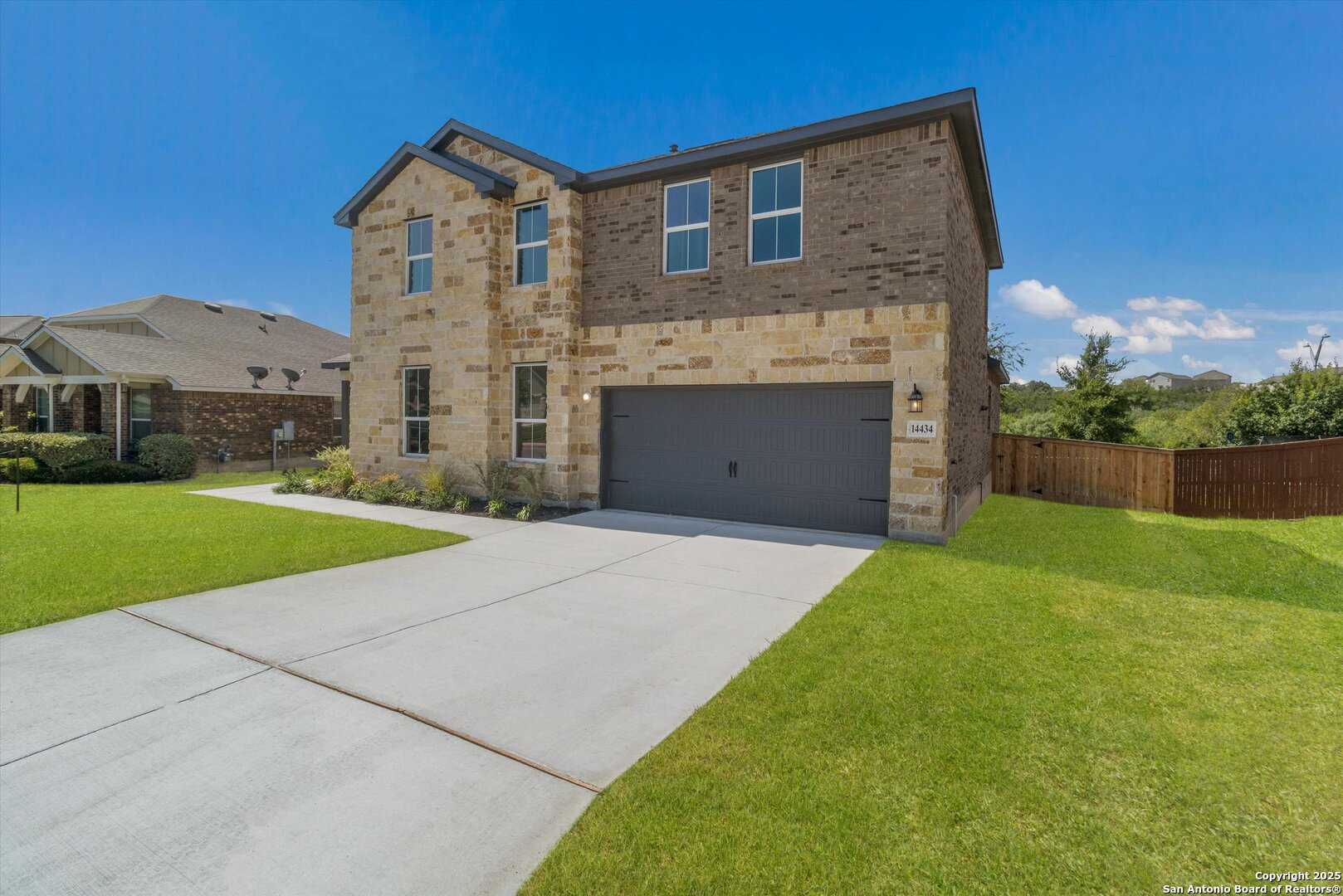 Modern two-story brick and stone home with two-car garage, driveway, and landscaped yard in Ladera, San Antonio, Texas