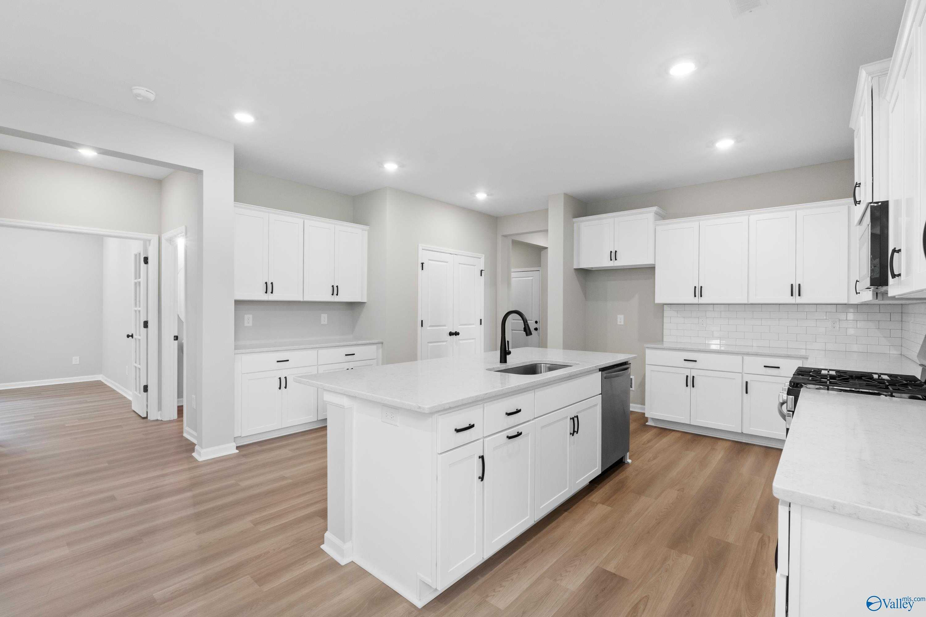 Modern white kitchen with quartz island, stainless sink, and subway tile backsplash in The Nantucket 3-bedroom home, Madison, Alabama