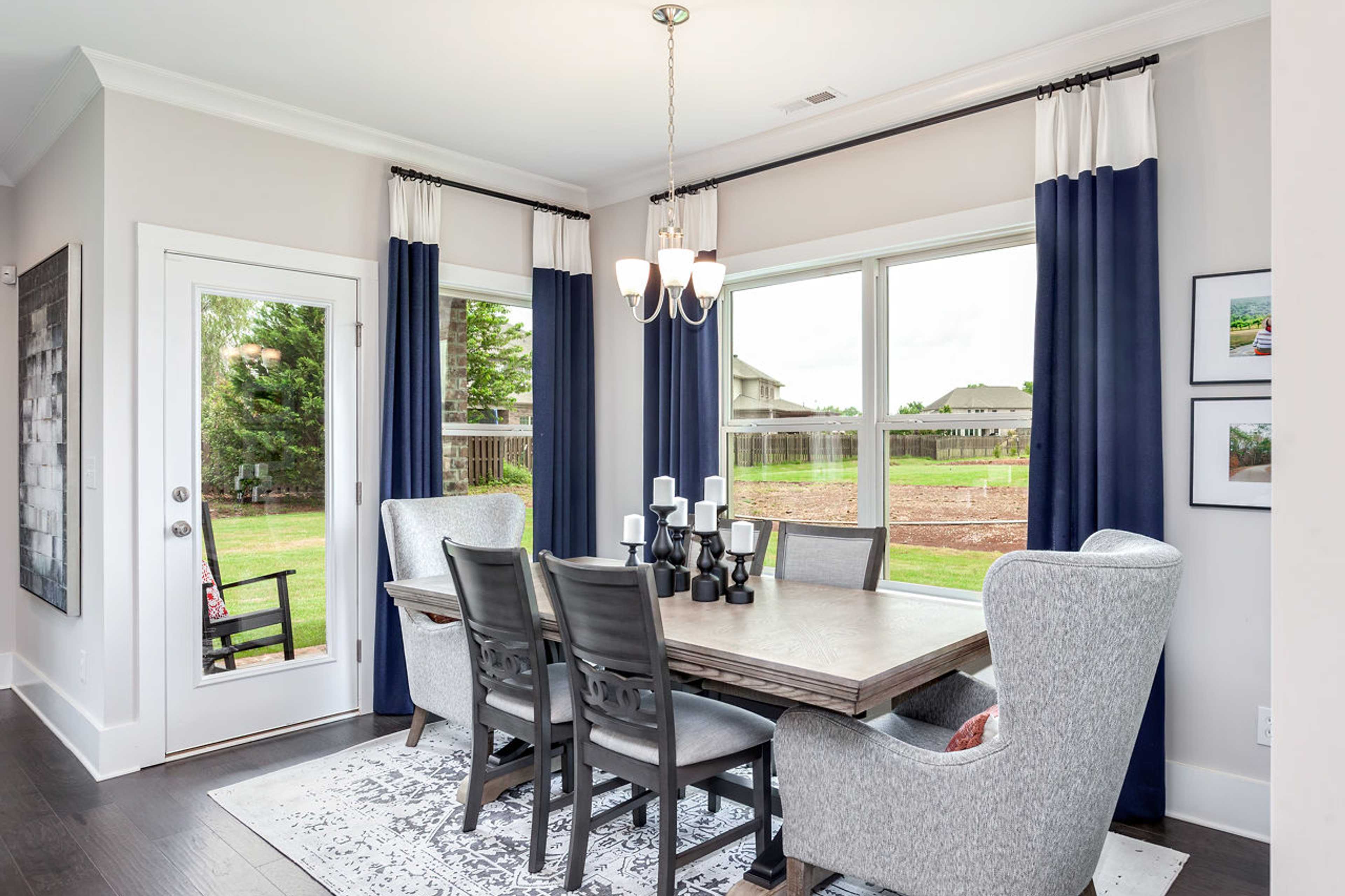 Elegant dining room at Williams Pointe in Huntsville AL with wooden table, gray wingback chairs, chandelier, and backyard view through navy curtains