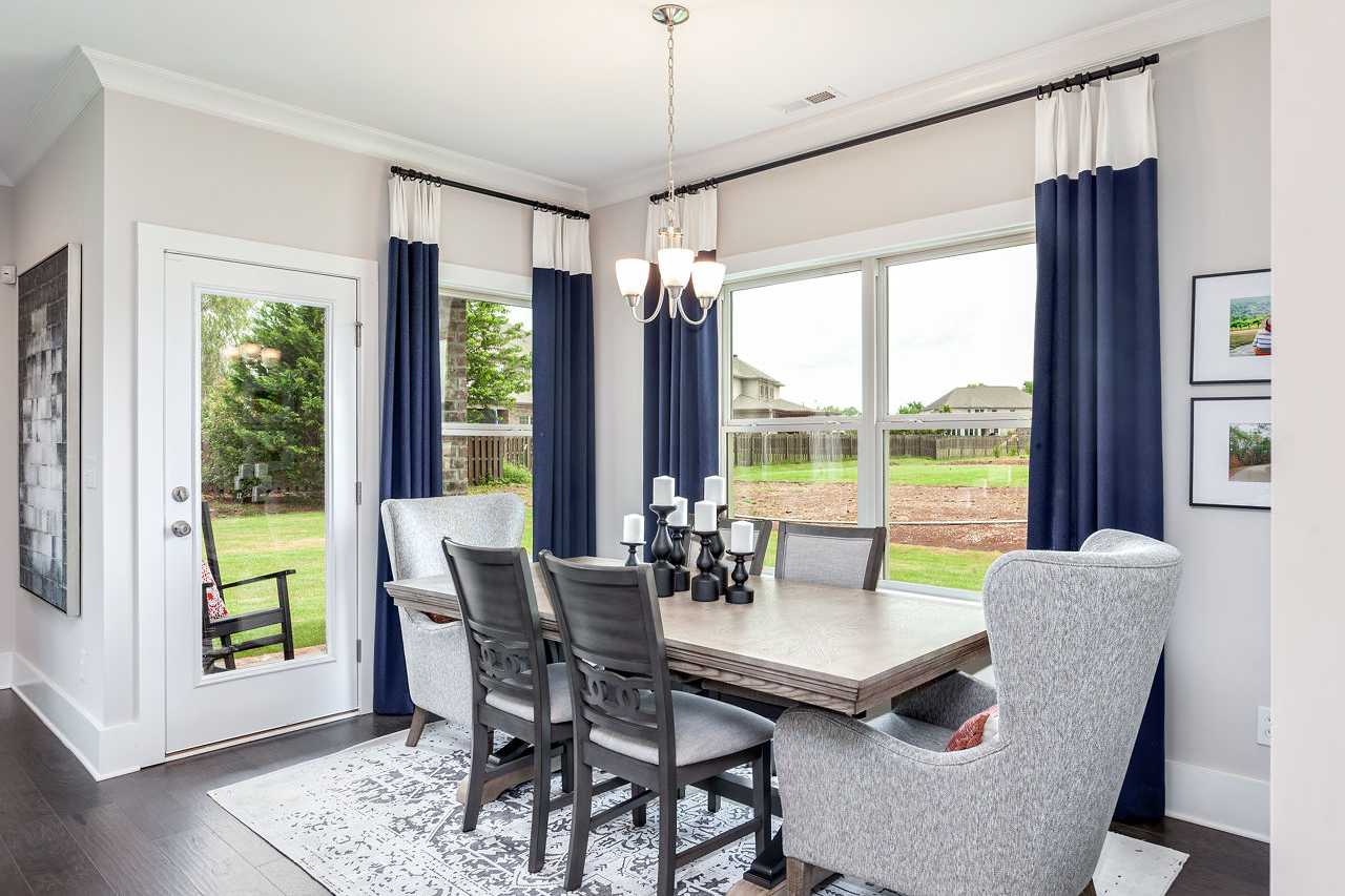 Elegant dining room at Williams Pointe in Huntsville AL with wooden table, gray wingback chairs, chandelier, and backyard view through navy curtains