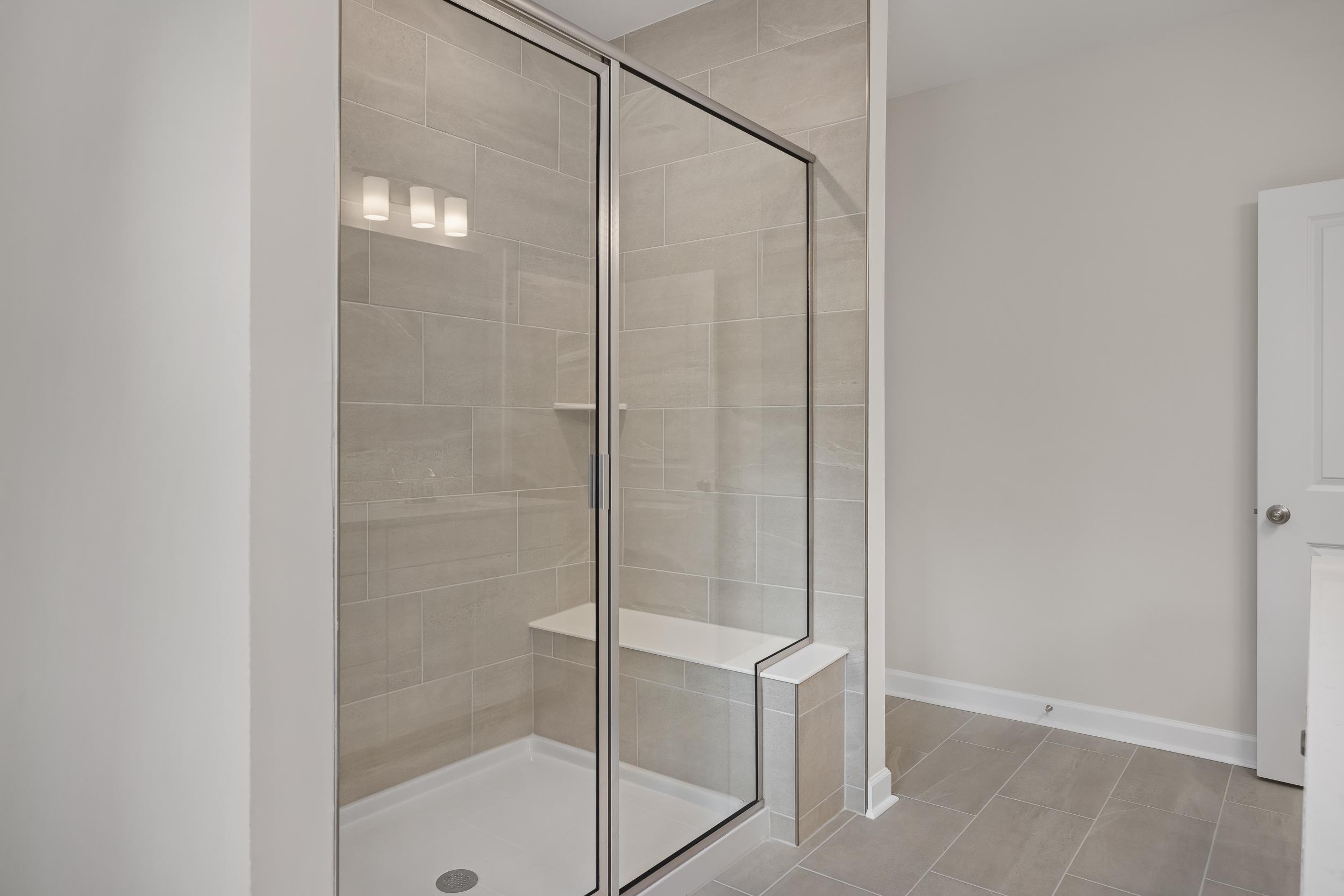 Modern master shower in The Beech A with frameless glass doors, subway tile walls, built-in bench, and sleek tile floor