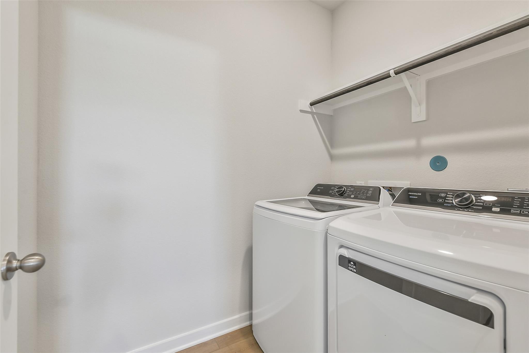 Modern laundry room with white front-load washer, dryer, and overhead shelves in Davidson Homes The Colorado F, Cleveland, Texas