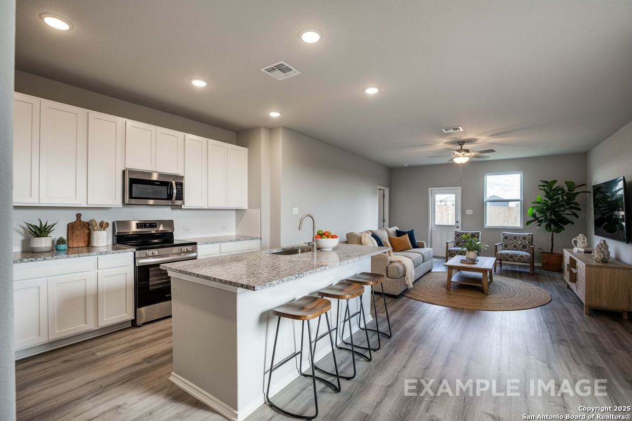 Open-concept kitchen-living area with white shaker cabinets, granite island, stainless appliances, cozy gray sofa in Davidson Homes The Blanco C, San Antonio