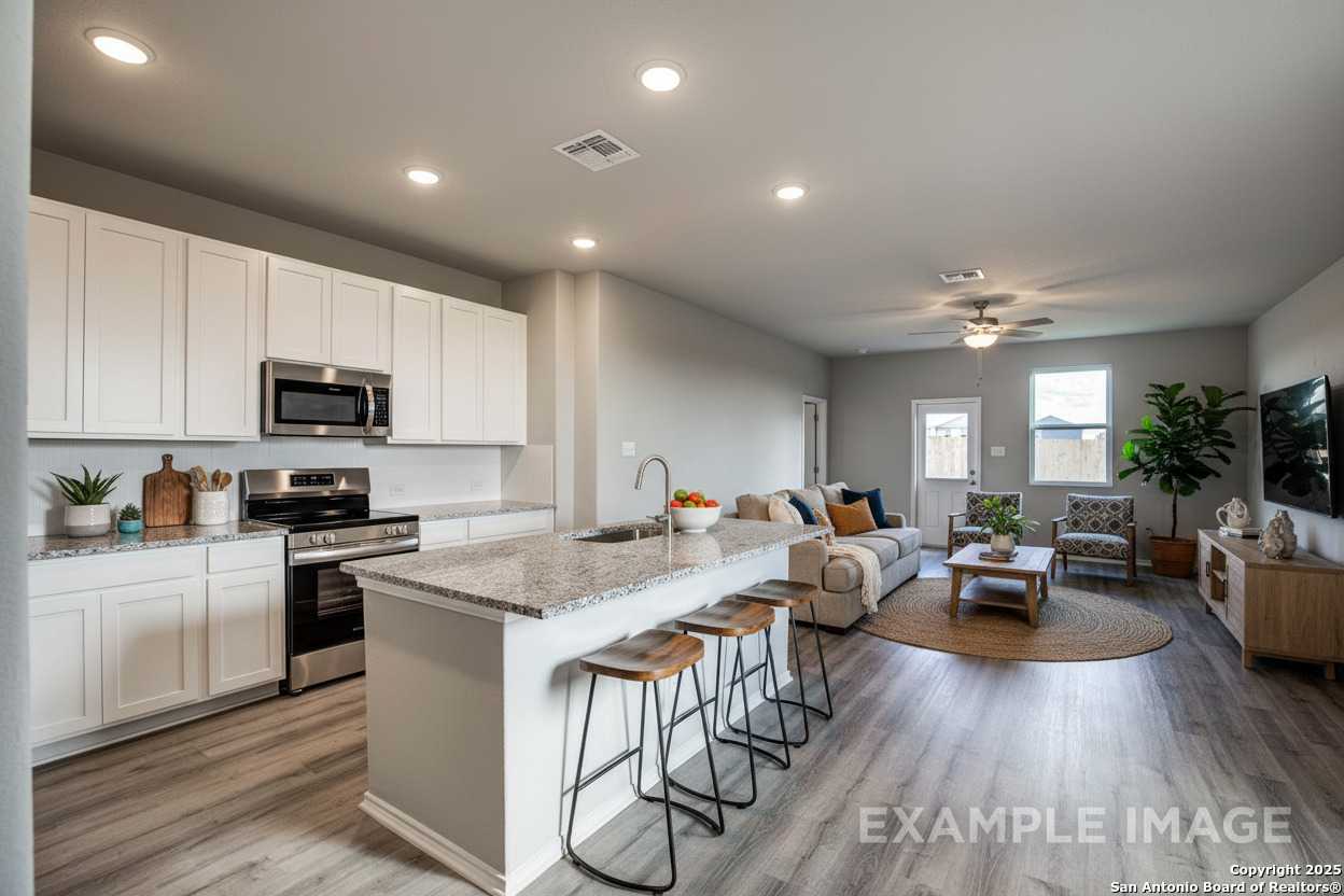 Open-concept kitchen-living area with white shaker cabinets, granite island, stainless appliances, cozy gray sofa in Davidson Homes The Blanco C, San Antonio
