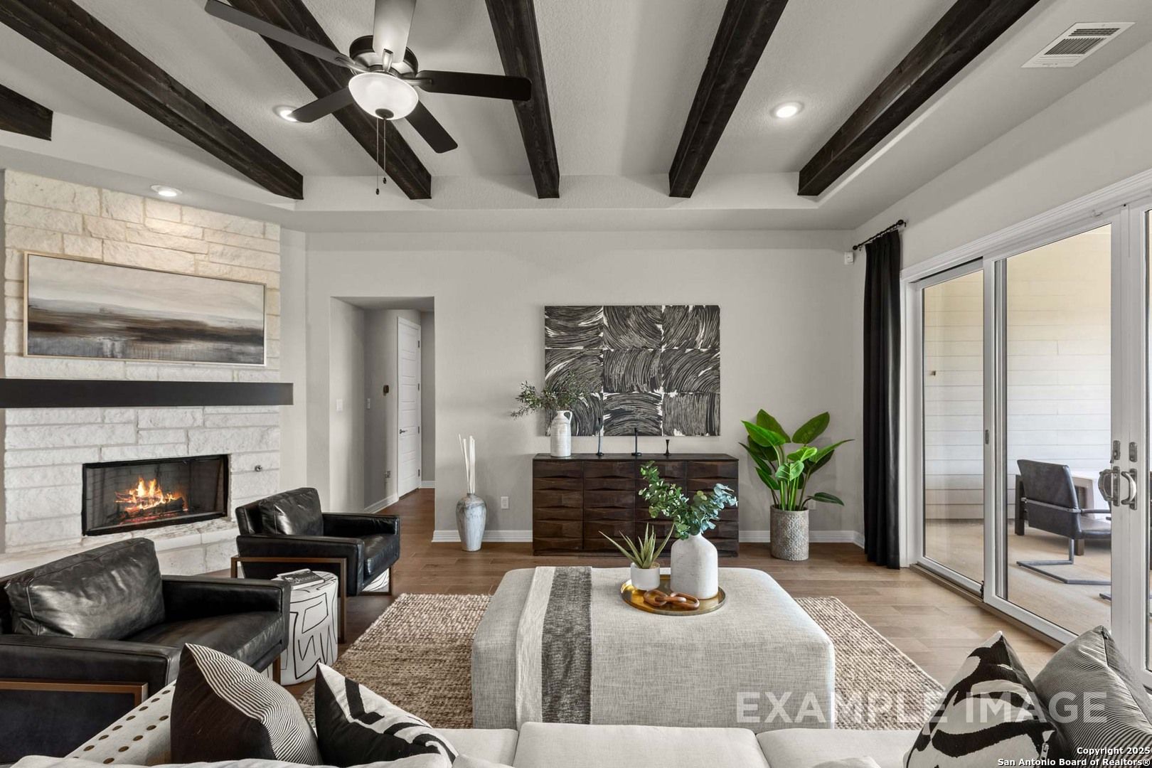 Cozy living room featuring stone fireplace, leather armchairs, beamed ceiling, and sliding doors to patio in Davidson Homes The Summerlin B, Castroville, Texas