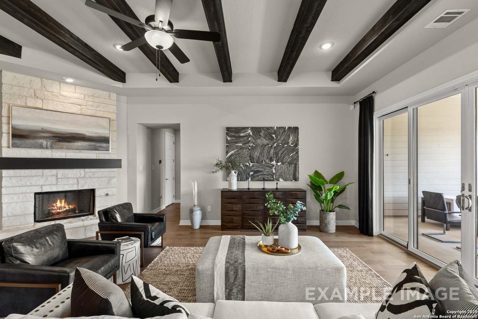 Cozy living room featuring stone fireplace, leather armchairs, beamed ceiling, and sliding doors to patio in Davidson Homes The Summerlin B, Castroville, Texas