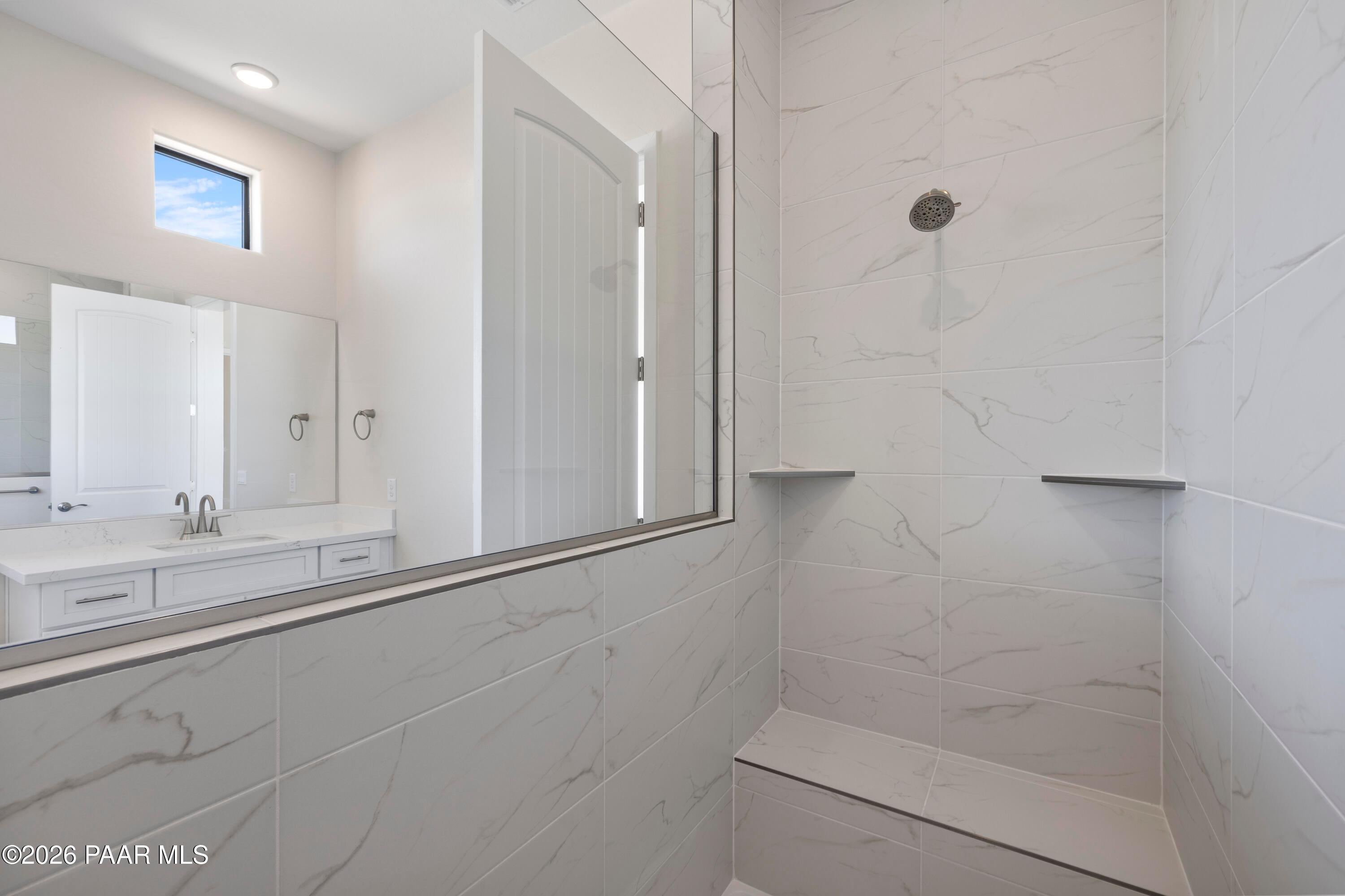 Modern master bathroom featuring white subway tile shower with bench, double white vanity, and large mirror in Davidson Homes The Soleil E, Prescott, Arizona