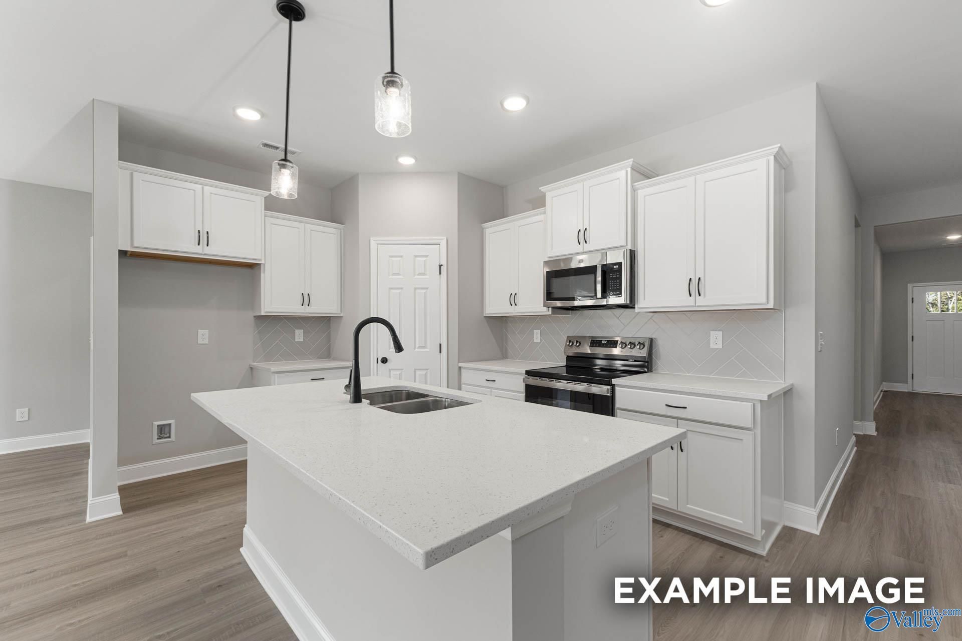 Modern white shaker kitchen with quartz island, stainless appliances, pendant lights in Davidson Homes Daphne D, Meridianville AL