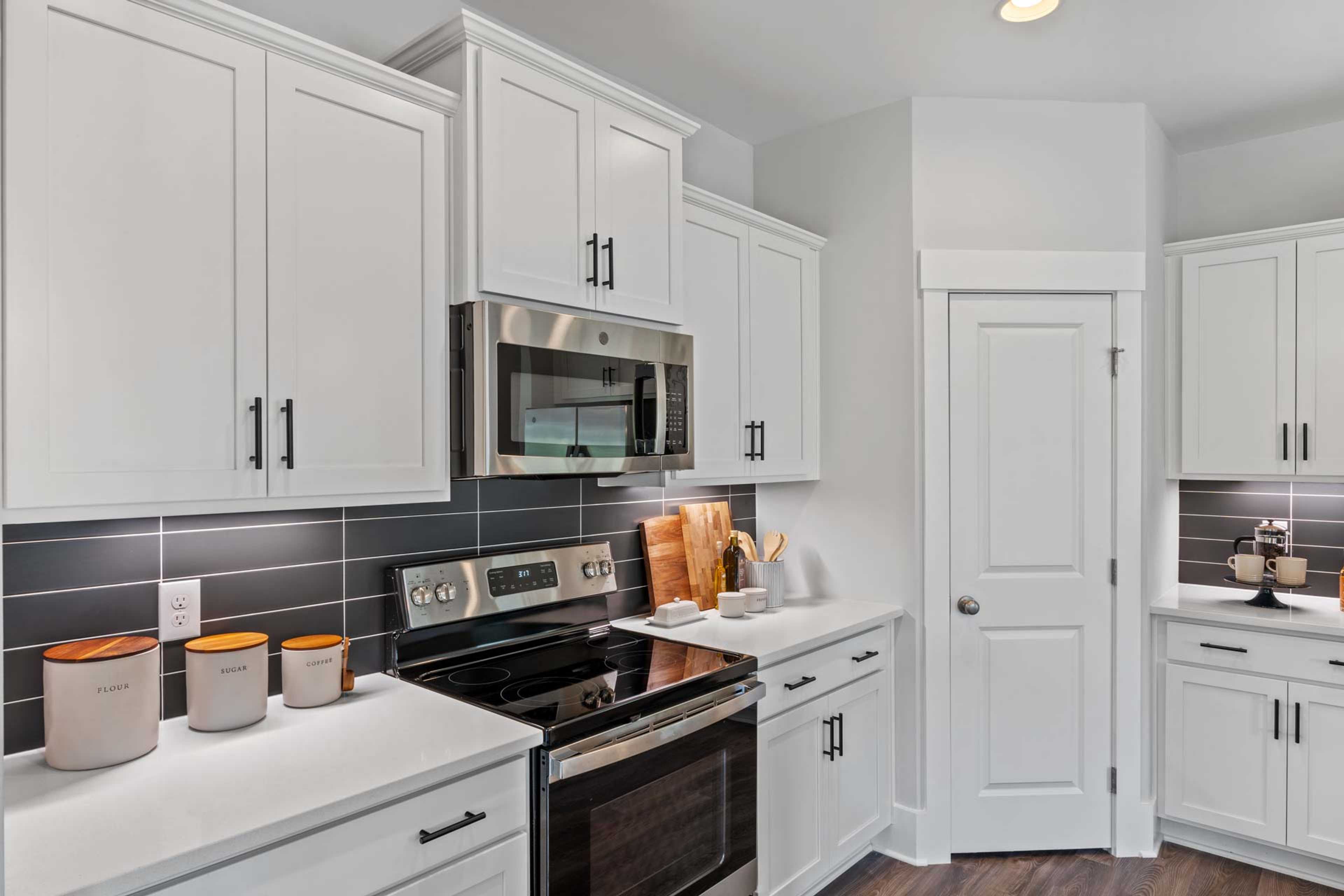 Contemporary kitchen in Blue Spring Huntsville AL with white shaker cabinets, stainless steel appliances, and dark subway tile backsplash