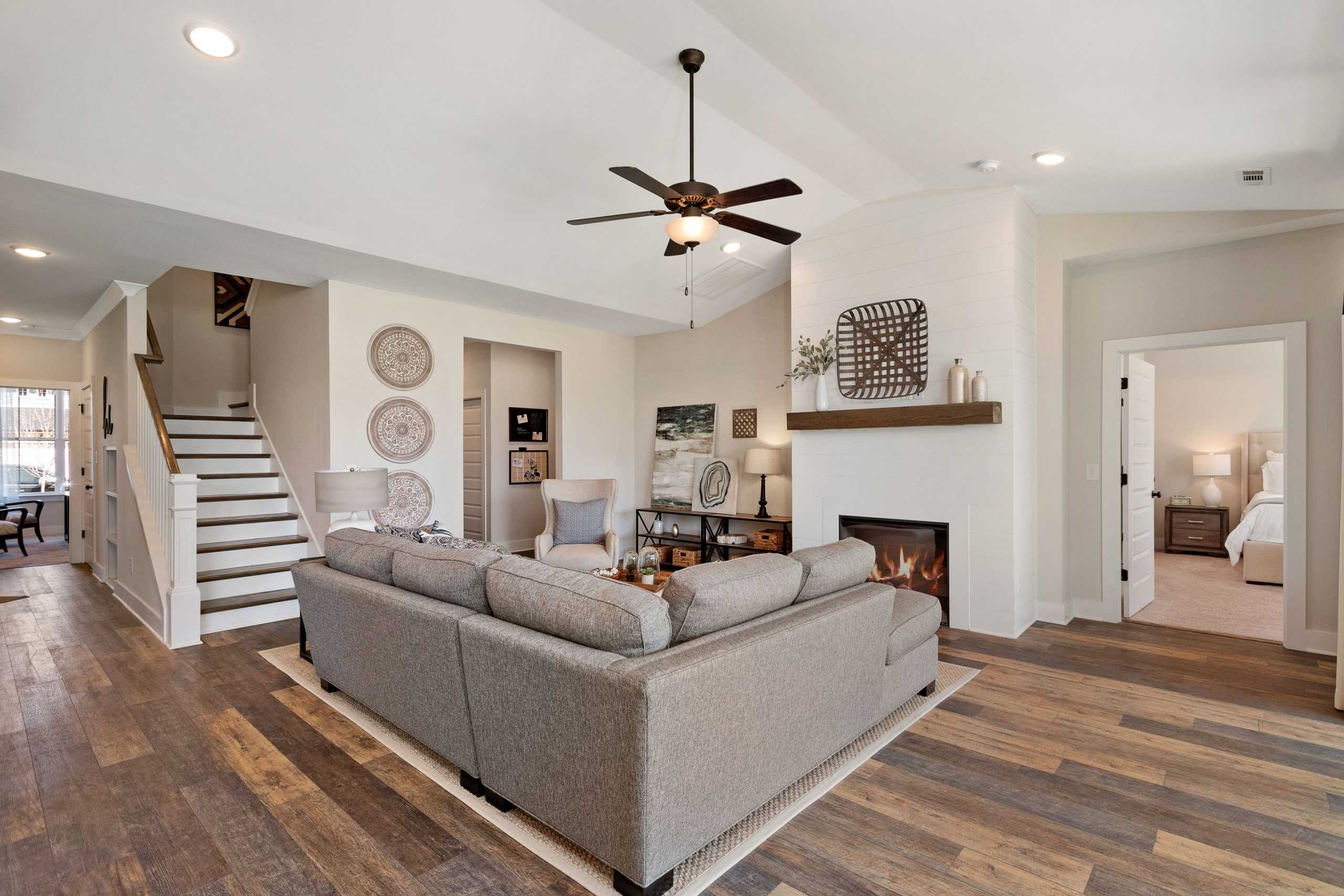Spacious open-concept living room in Rivers Edge Murfreesboro TN featuring gray sectional sofa, white brick fireplace, hardwood floors