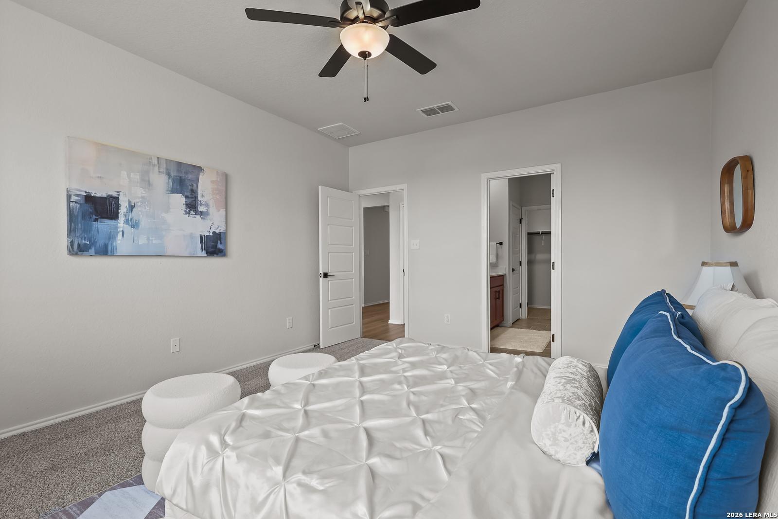 Cozy gray bedroom with white tufted bed, blue pillows, abstract art, ceiling fan, and en-suite bath in Davidson Homes The Daphne H, Seguin, Texas