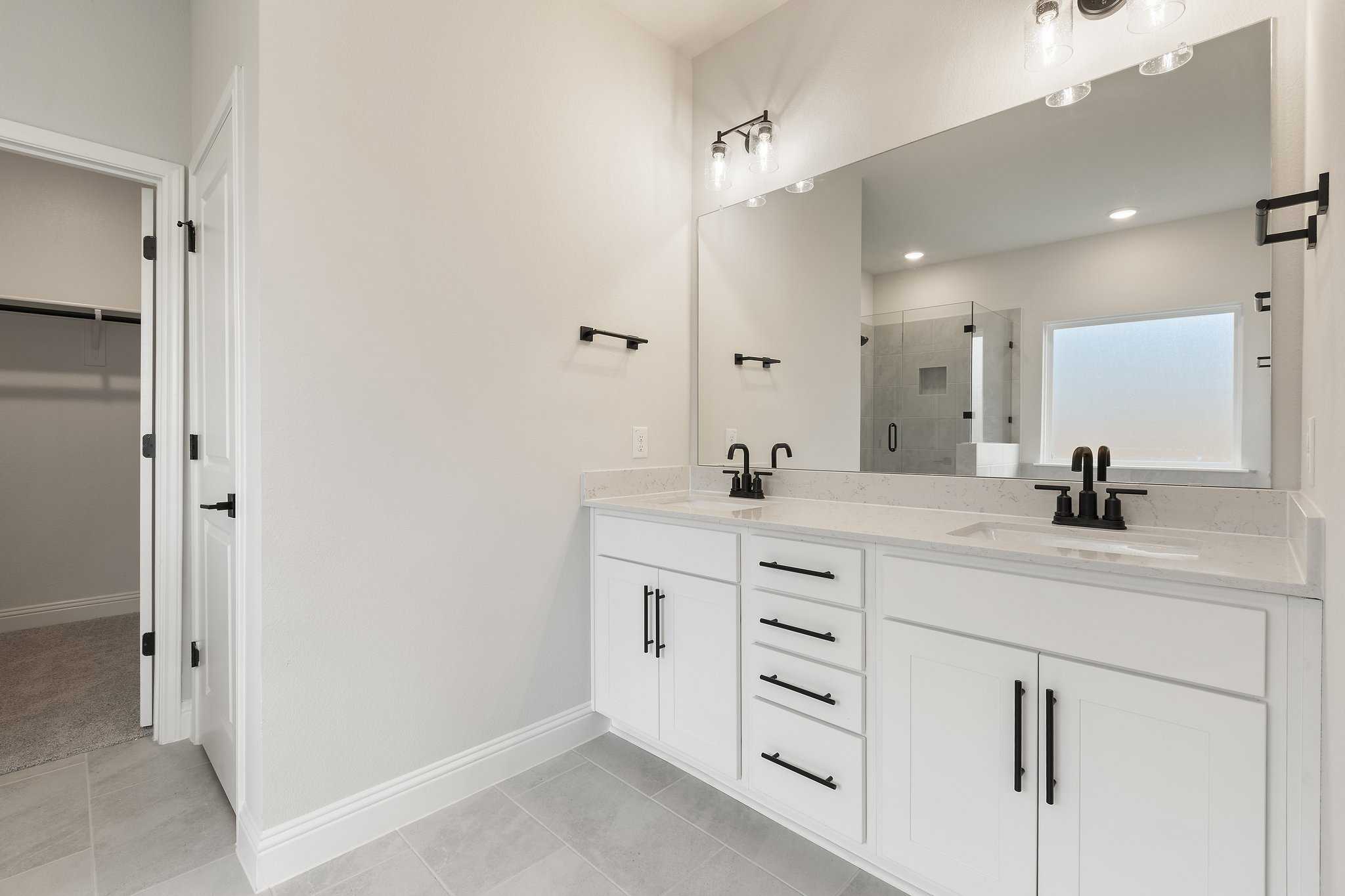 Modern master bathroom in The Harrison featuring white double vanity, large mirror, and frameless glass shower