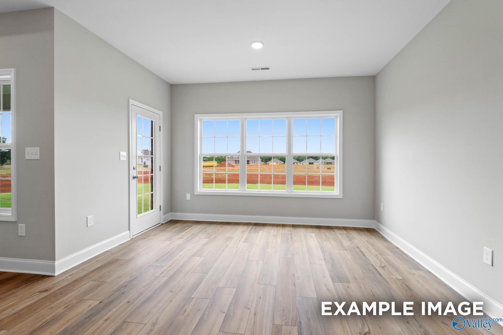 Bright living room with large windows overlooking green field and hardwood floors in Davidson Homes The Finleigh, Harvest, AL