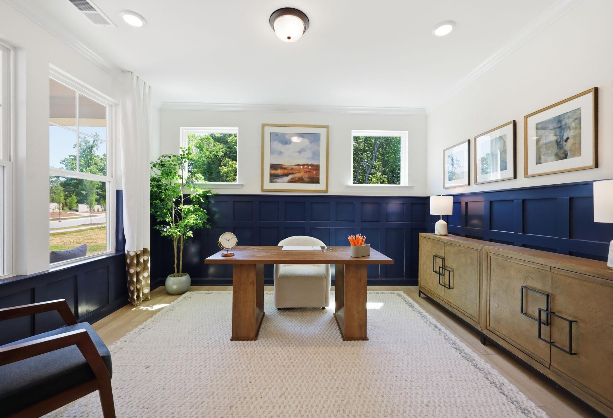 Bright home office in The Aspen floor plan featuring navy blue wainscoting, a wood desk, and modern decor.