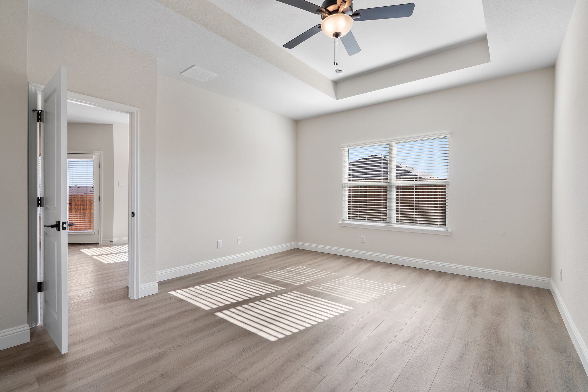 Spacious master bedroom in The Holly F floor plan featuring a tray ceiling, ceiling fan, and light wood-style flooring.