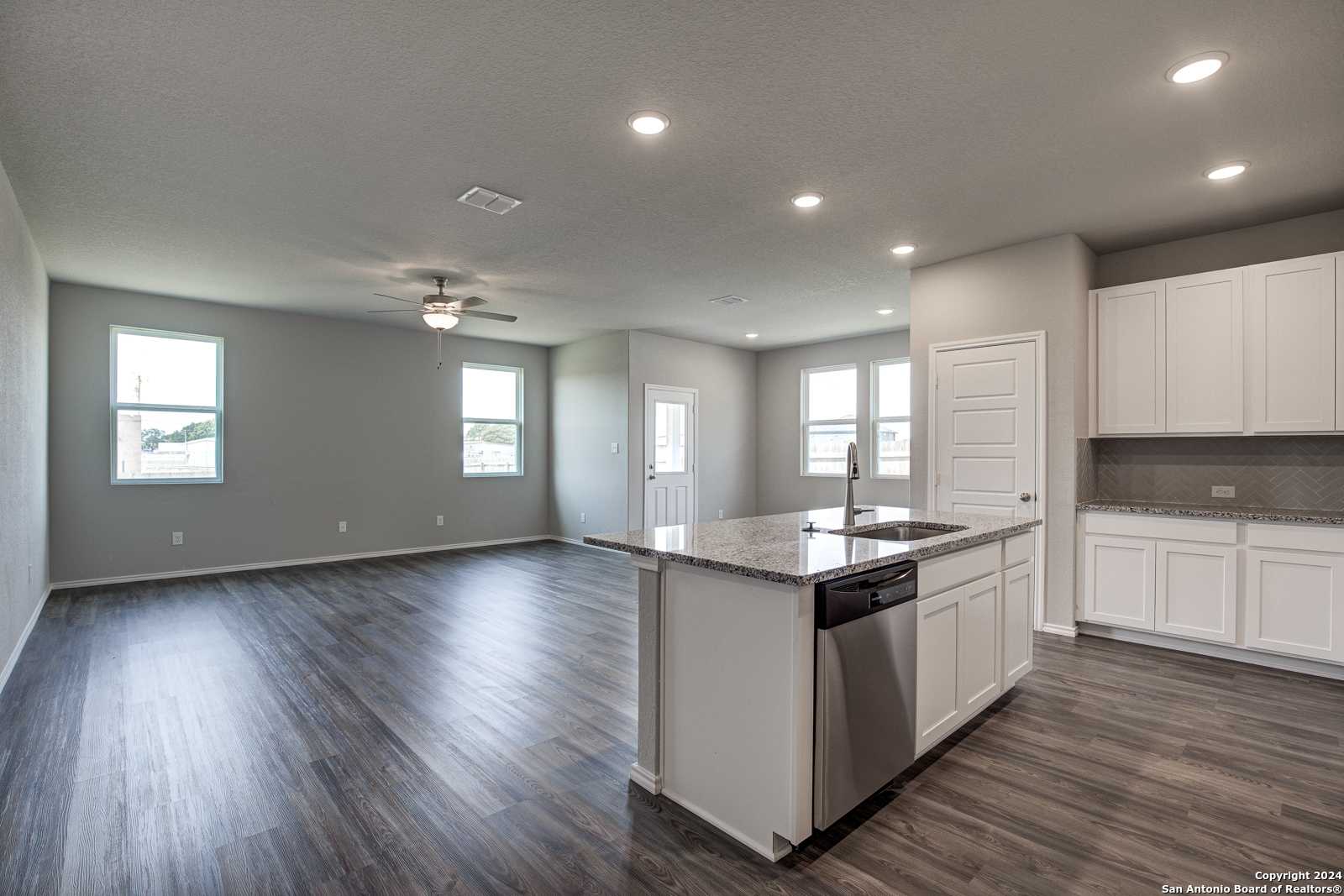 Spacious open-concept kitchen-living area with granite island, white cabinets, stainless dishwasher, hardwood floors in The Daphne J, Seguin TX