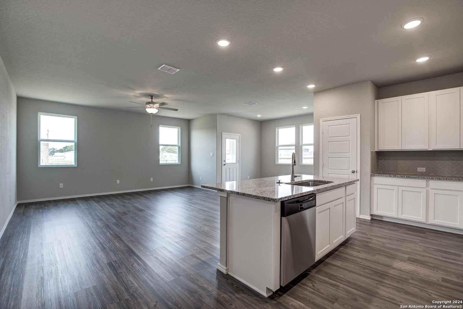 Spacious open-concept kitchen-living area with granite island, white cabinets, stainless dishwasher, hardwood floors in The Daphne J, Seguin TX