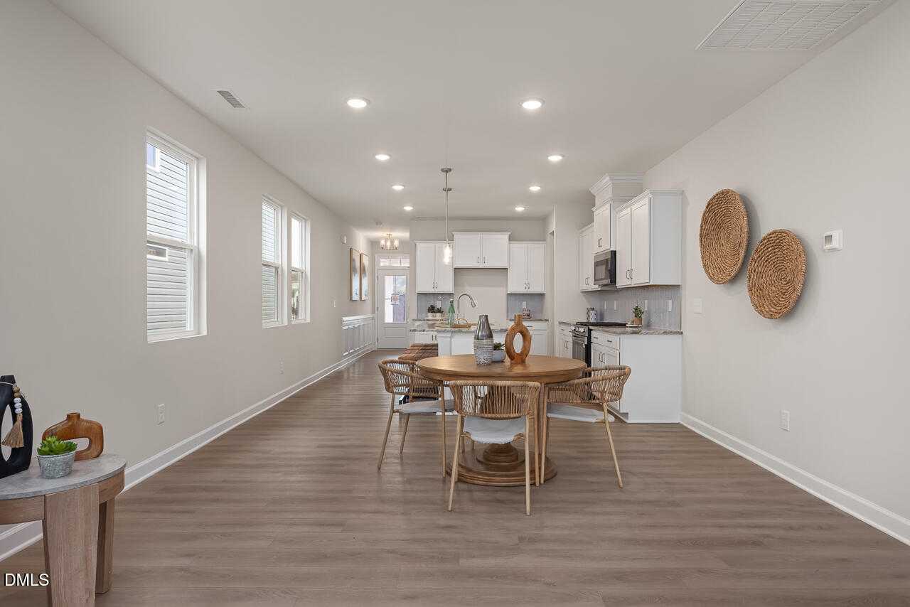 Modern open-concept kitchen with white cabinets, island sink, and dining nook featuring round rattan table in The Carter C, Lillington, NC