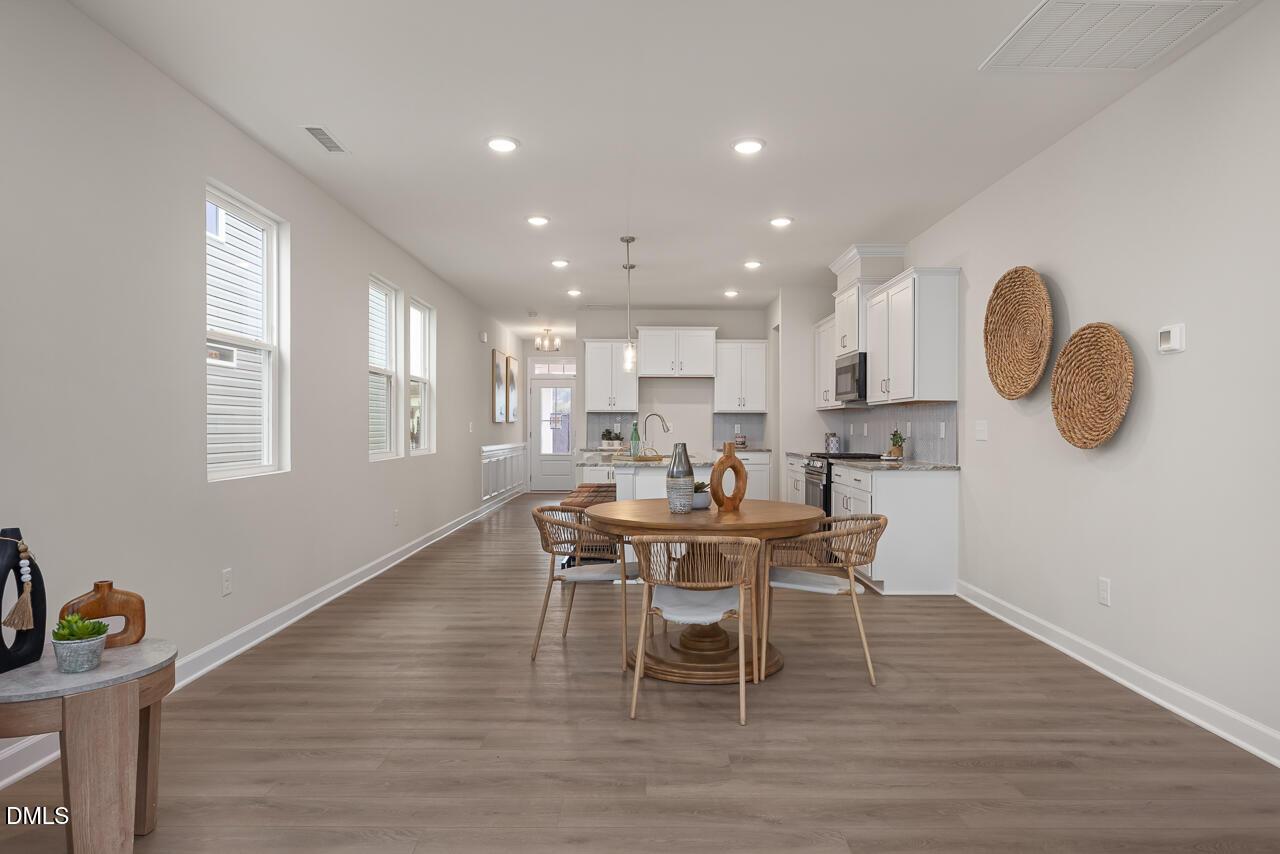 Bright open-concept kitchen and dining area with round rattan table, white cabinets, and woven decor in Davidson Homes The Carter C, Lillington NC