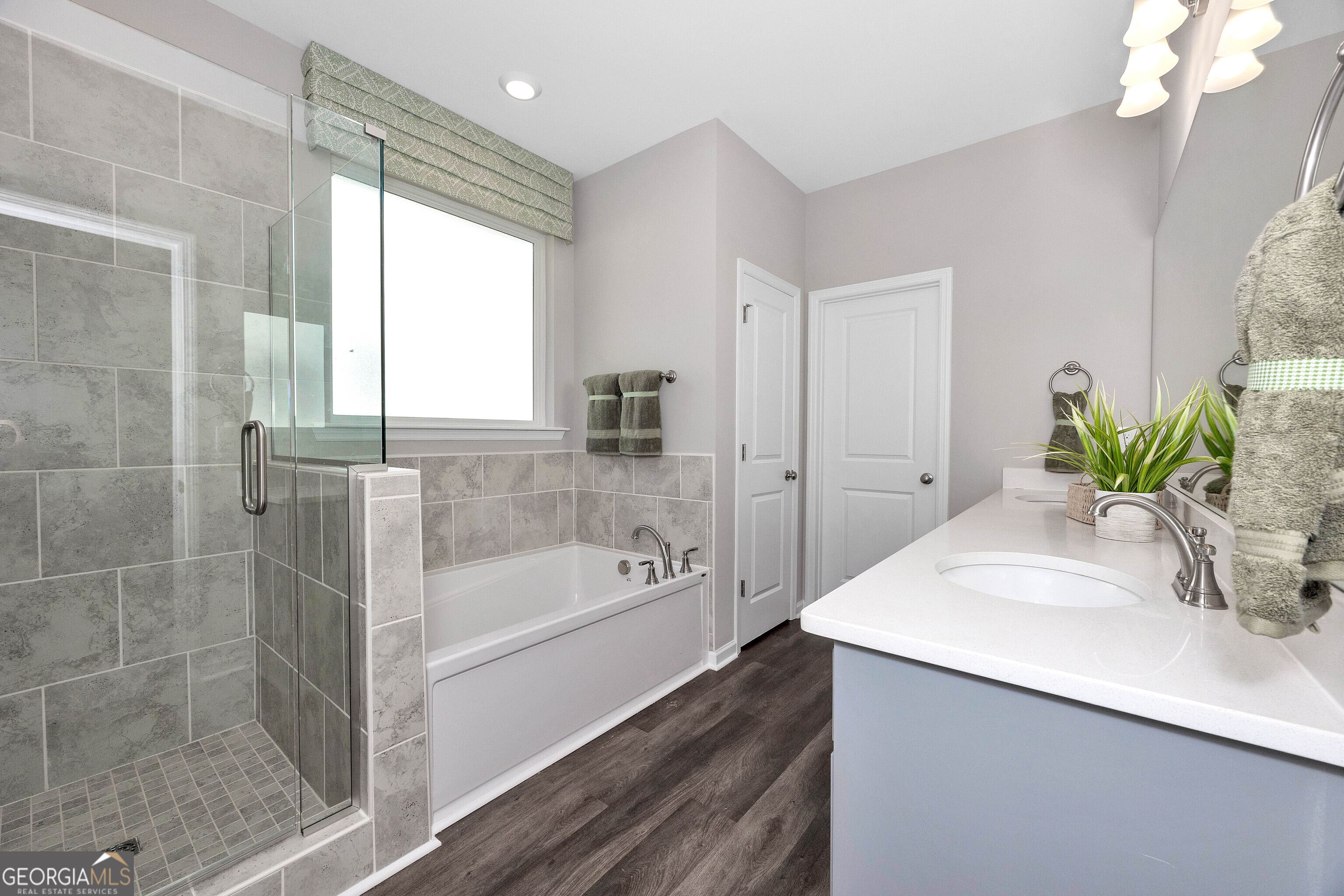 Elegant master bath with glass shower, soaking tub, double vanity, and gray tiles in Evermore Homes The Stella, Perry, GA