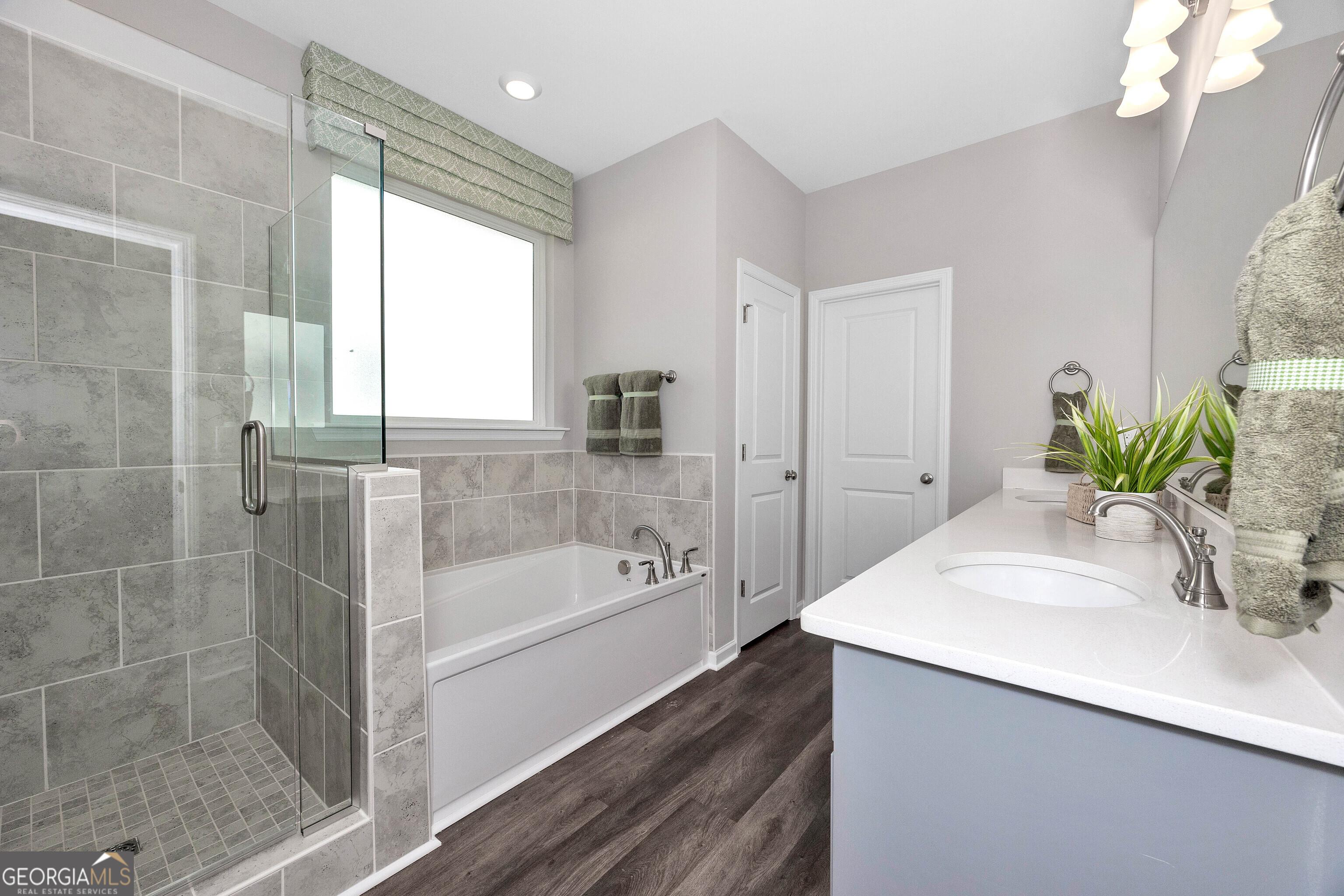 Elegant master bath with glass shower, soaking tub, double vanity, and gray tiles in Evermore Homes The Stella, Perry, GA