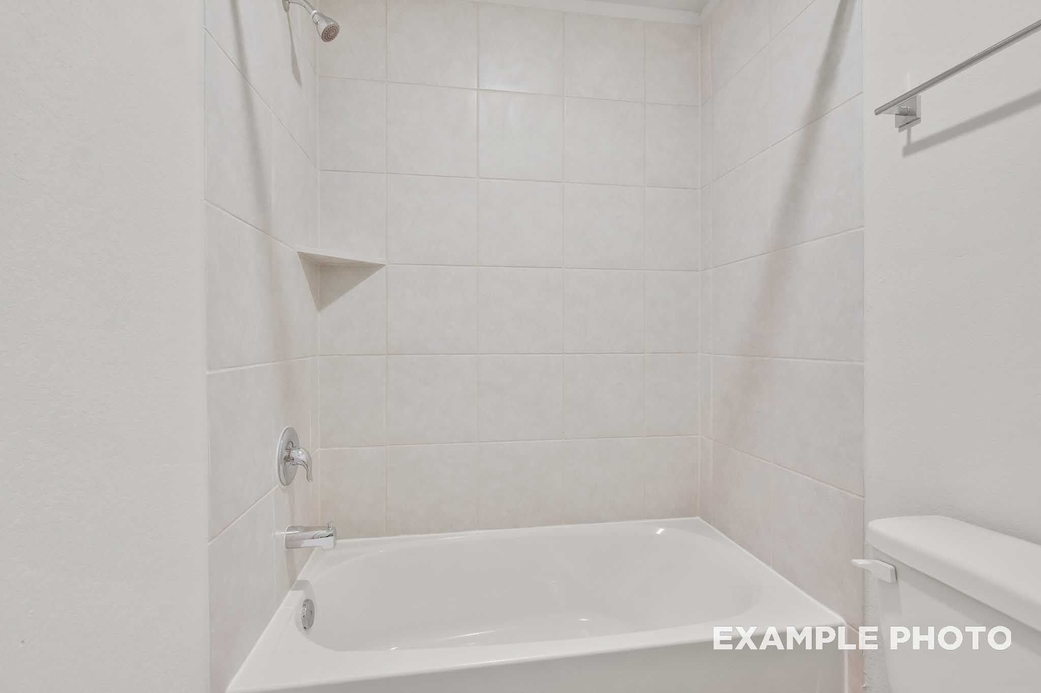 White tile bathtub shower with chrome fixtures in The Brazos by Davidson Homes, new construction home in Beasley, Texas.