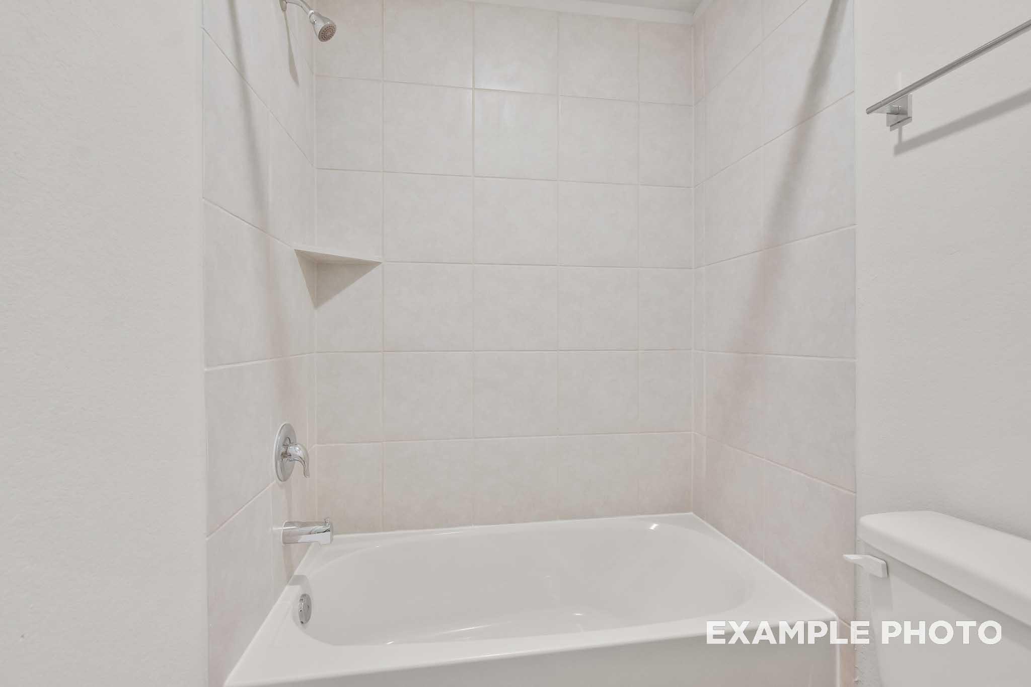 White tile bathtub shower with chrome fixtures in The Brazos by Davidson Homes, new construction home in Beasley, Texas.