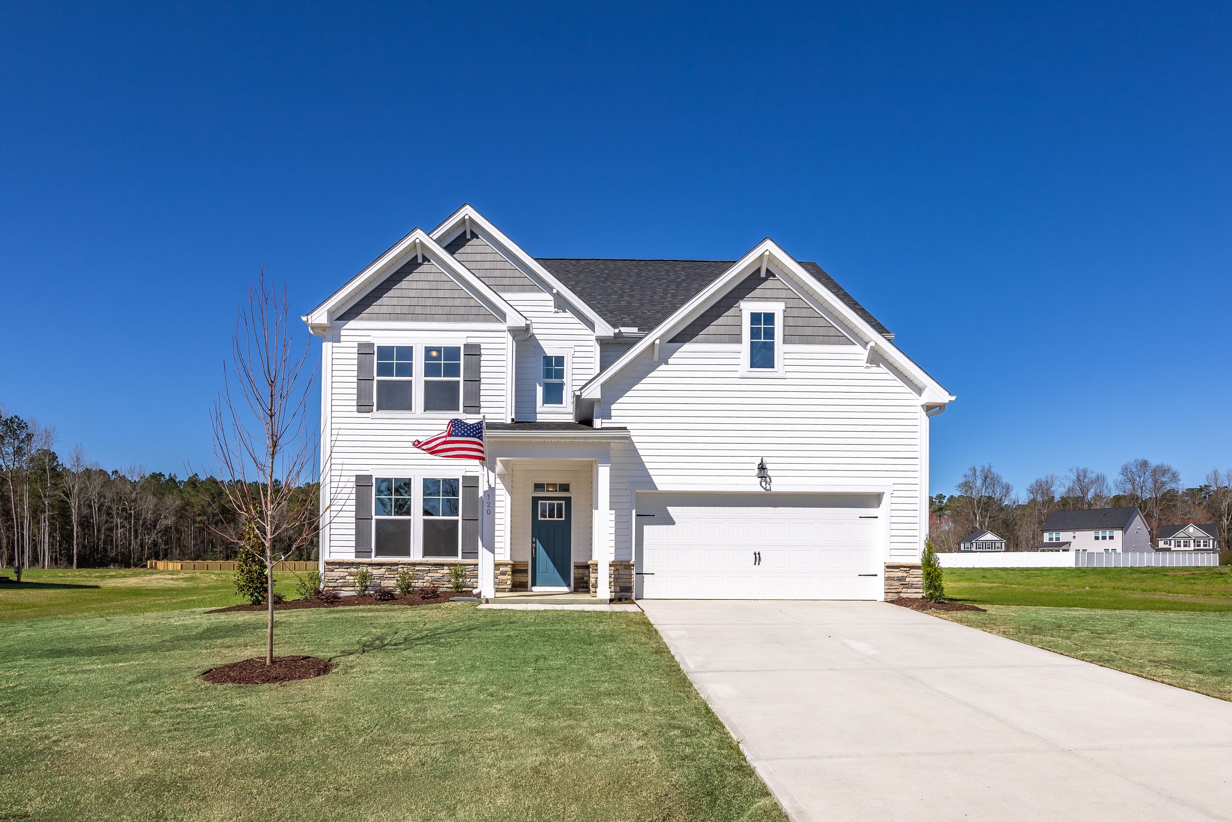 Two-story white craftsman home exterior at Montrose in Aberdeen NC with covered porch, American flag, garage and landscaped yard