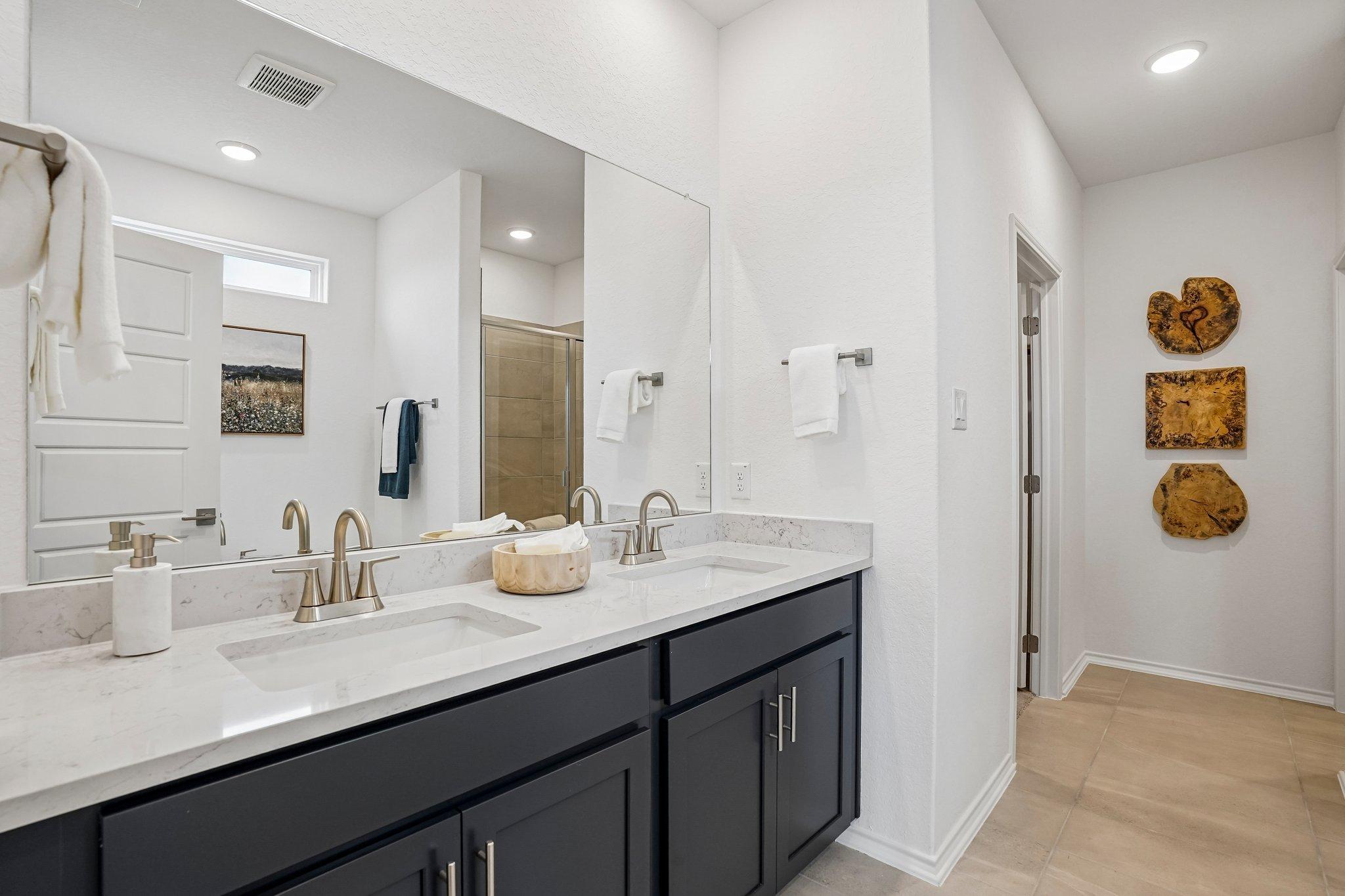 Modern primary bathroom with double vanity, quartz countertops, and dark cabinetry at Morgan Meadows in San Antonio, Texas.