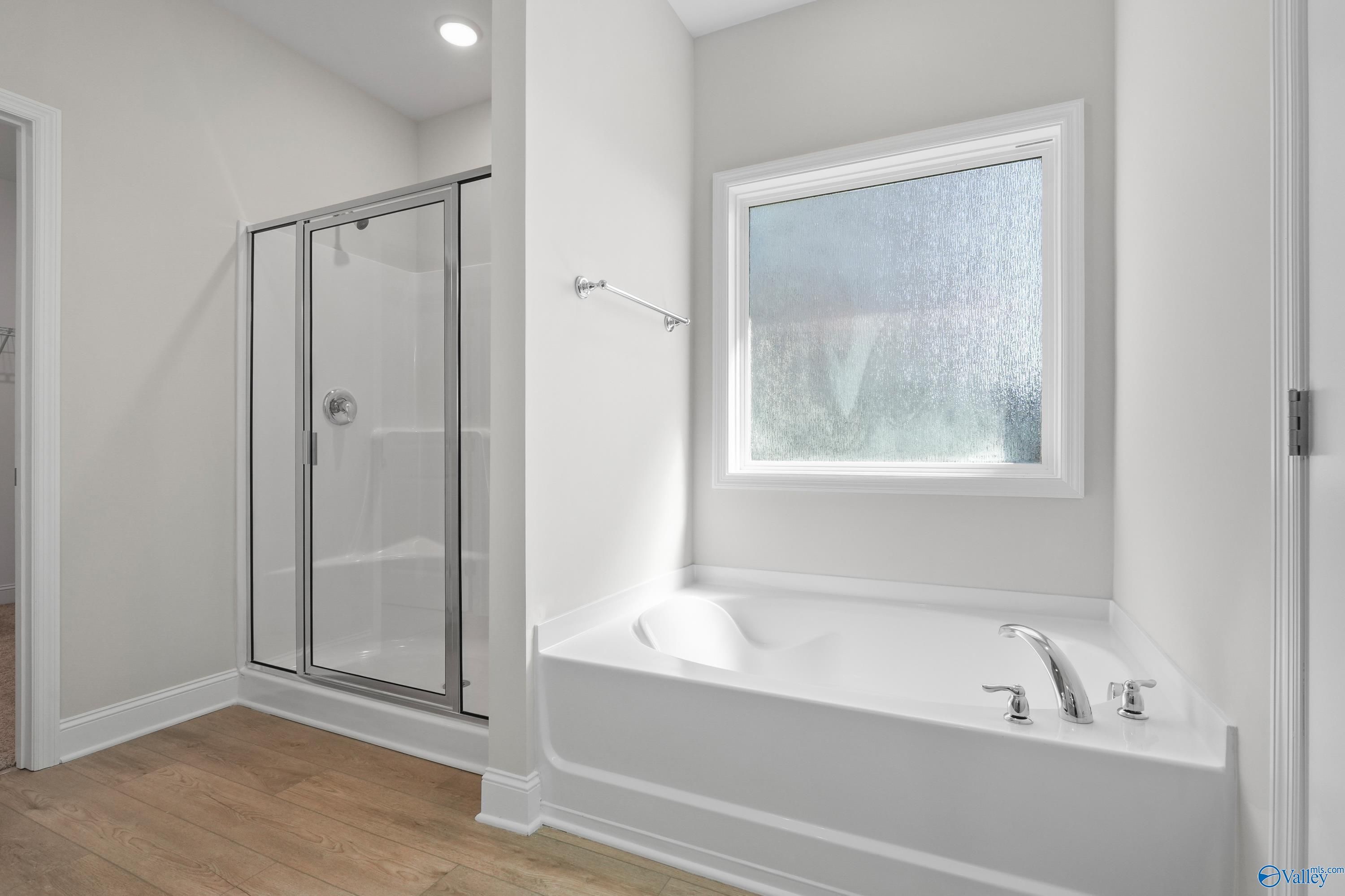Modern master bathroom featuring glass shower enclosure, white soaking tub, and frosted window in Davidson Homes The Everett, Hazel Green, Alabama