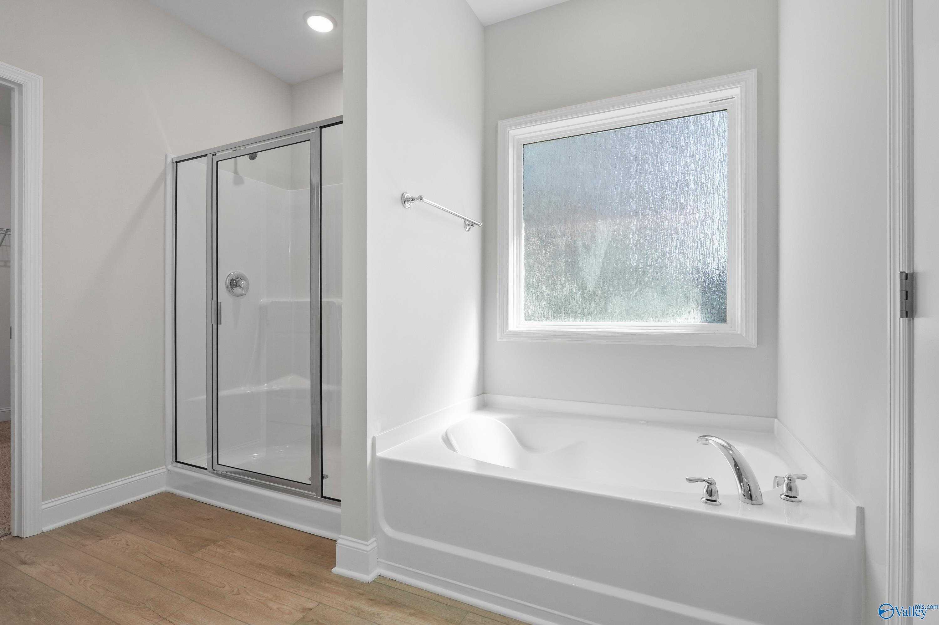 Modern master bathroom featuring glass shower enclosure, white soaking tub, and frosted window in Davidson Homes The Everett, Hazel Green, Alabama