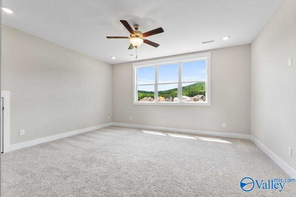 Bright empty bedroom with large windows overlooking green hills, ceiling fan, neutral walls in The Oxford 5-bedroom home, Owens Cross Roads, Alabama