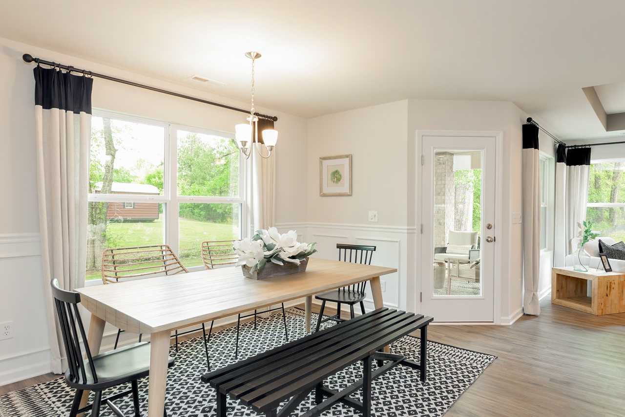 Spacious dining room in The Franklin home featuring farmhouse wooden table, black benches, large sunlit windows, and French doors