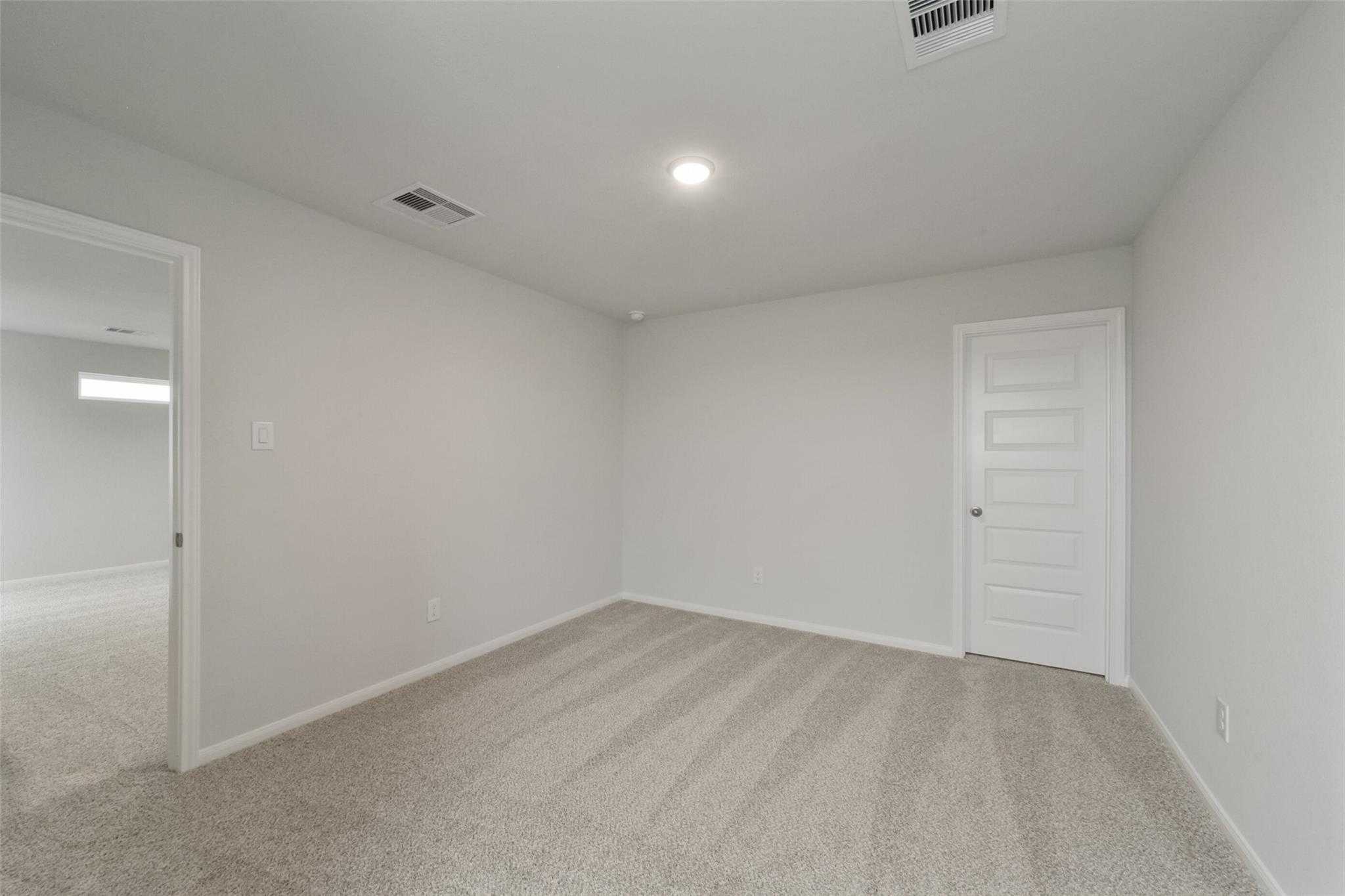 Empty secondary bedroom with beige carpet, white walls, and ample space in Davidson Homes The San Marcos E, Beasley, Texas