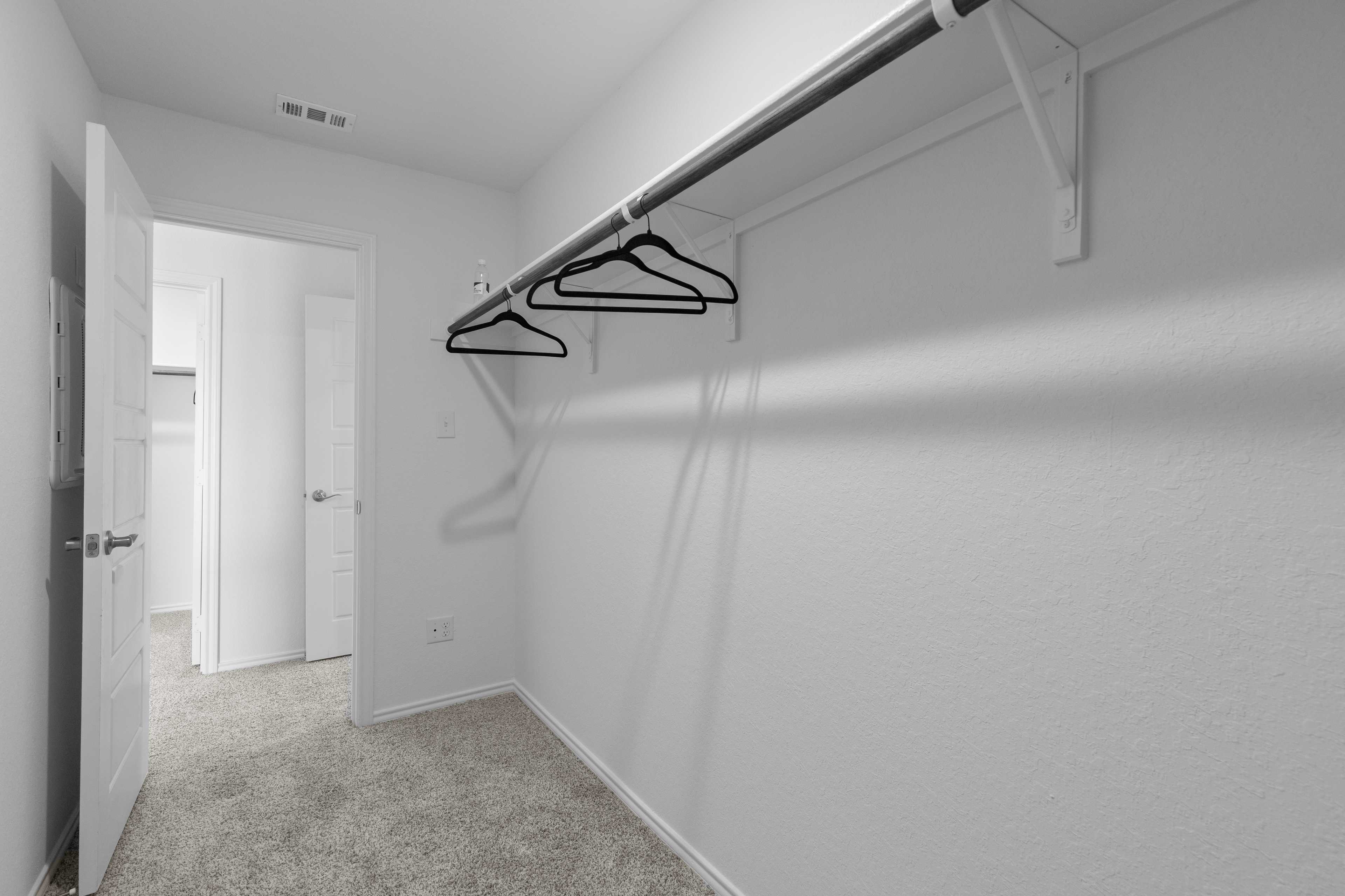 Spacious walk-in closet at Horizon Pointe in Converse Texas by Davidson Homes with white walls, hanging rods and carpet floor