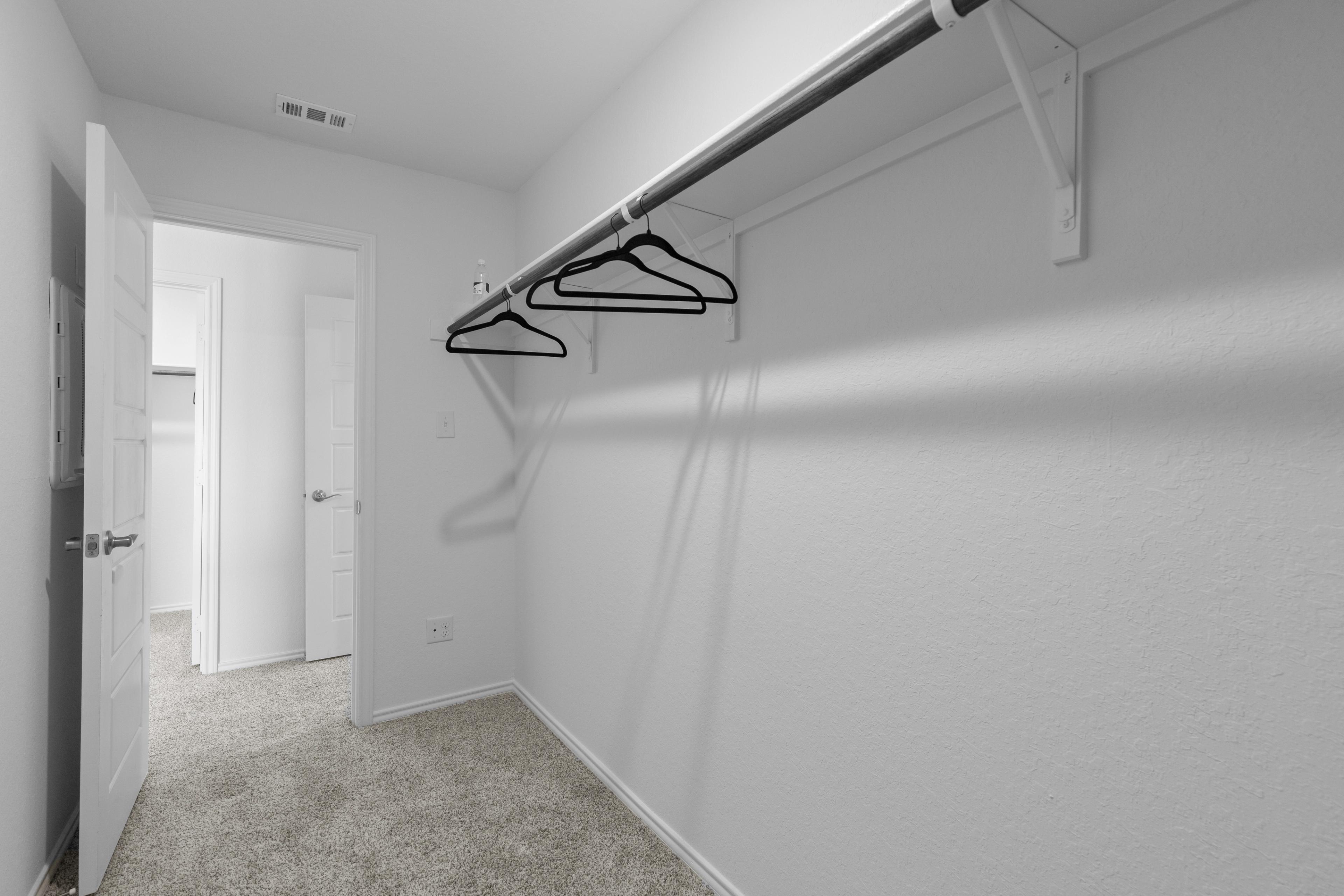 Spacious walk-in closet at Horizon Pointe in Converse Texas by Davidson Homes with white walls, hanging rods and carpet floor