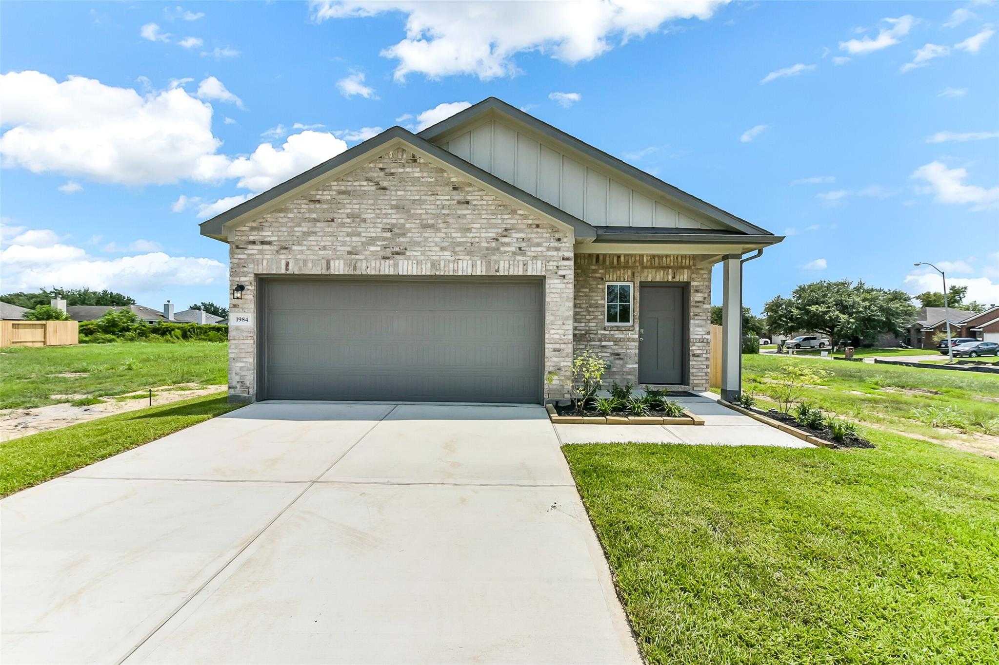 Brick single-story home with 2-car garage, driveway, and landscaped yard in The Villages at WestPointe, Dayton, Texas