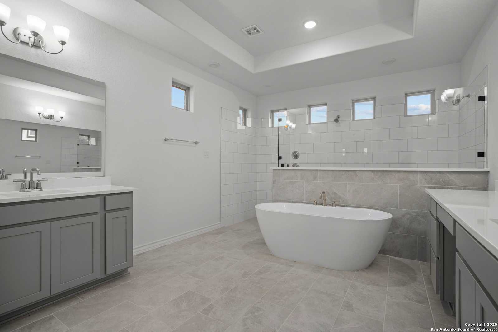 Elegant master bathroom with freestanding soaking tub, dual gray vanity, tiled shower in Davidson Homes Summerlin B, Castroville TX