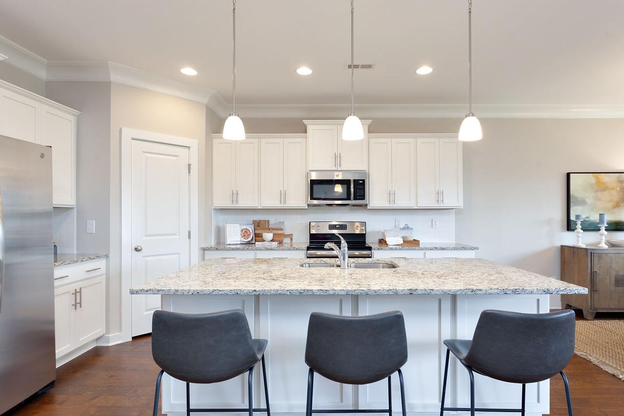 Modern kitchen at Laurenwood Preserve in Madison Alabama with white cabinets, granite island, stainless appliances, and bar stools