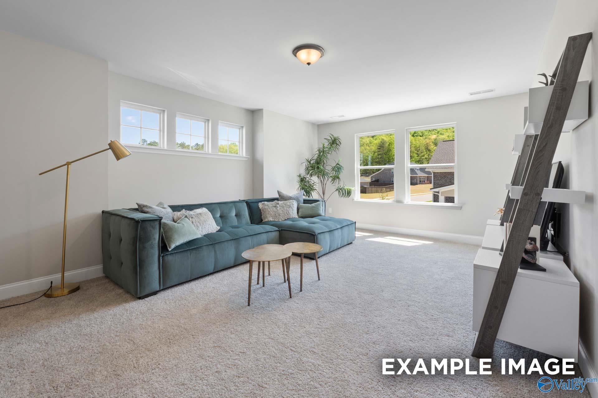 Cozy bonus room with teal velvet L-shaped sofa, gold lamp, ladder shelf, potted plant, and scenic windows in Evermore Homes The Haven E, Owens Cross Roads