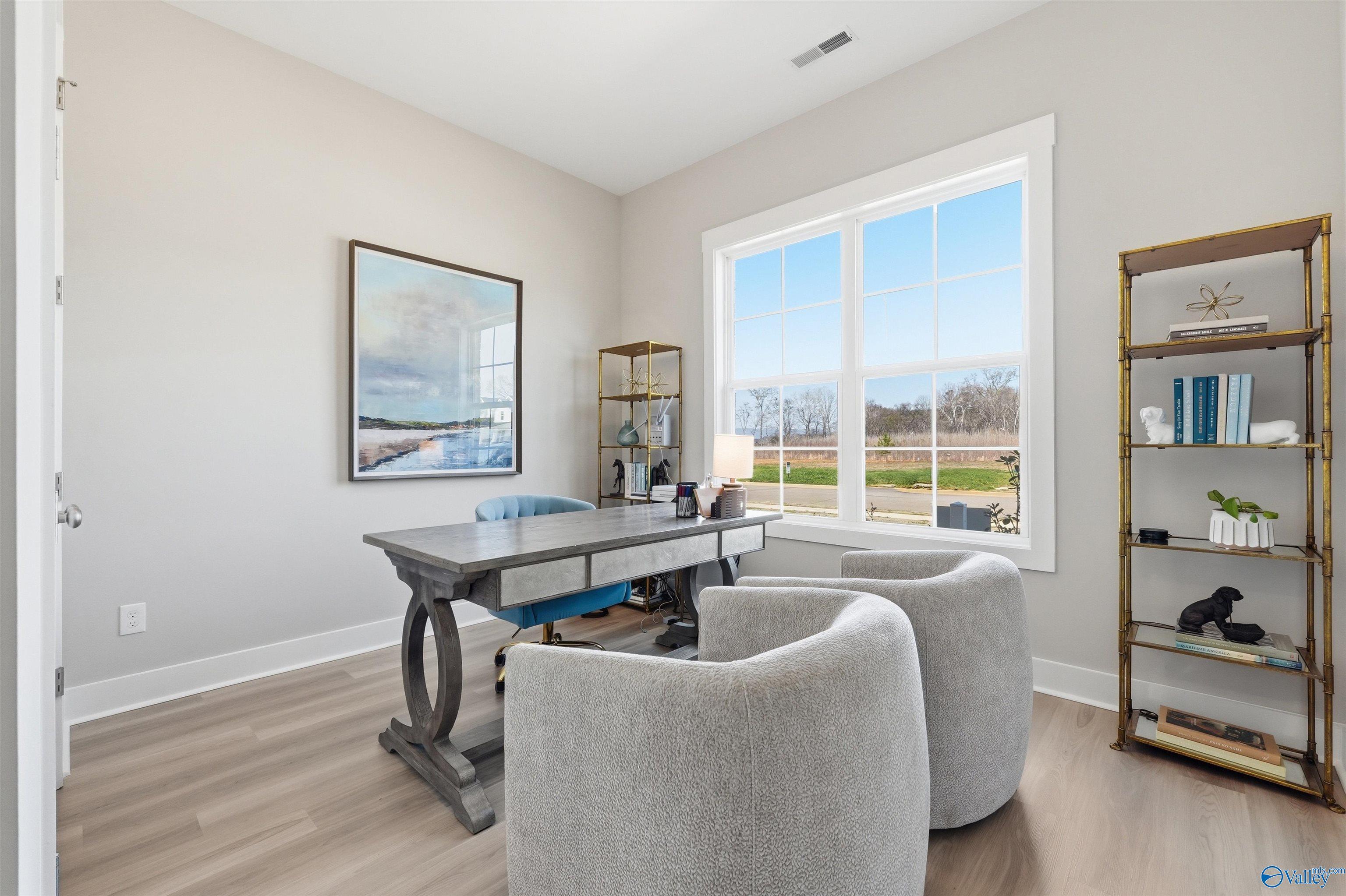 Elegant home office with wooden desk, blue chair, gray armchairs, gold bookshelf, and scenic window view in Evermore Homes Oxford B, Owens Cross Roads, Alabama
